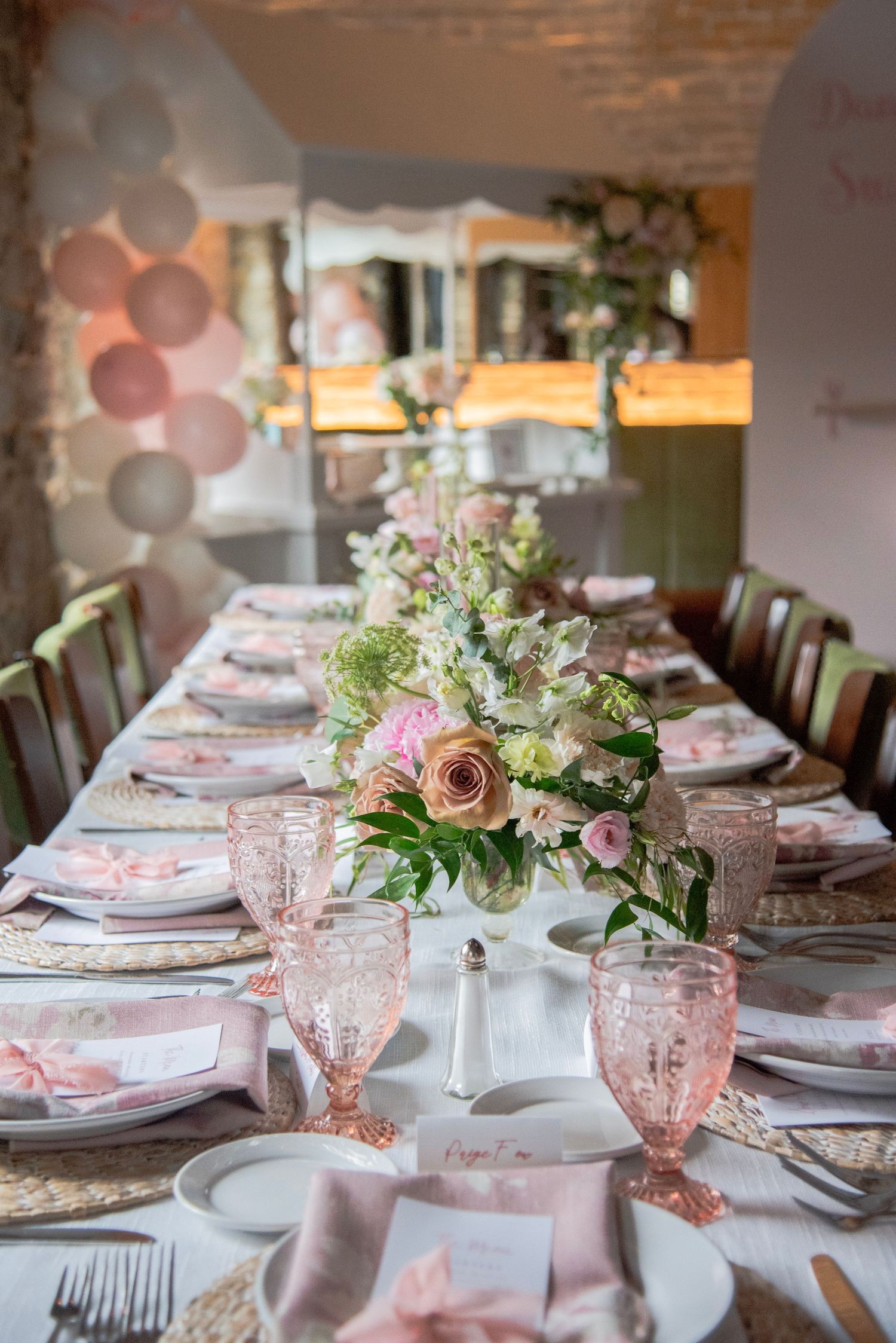 Elegant table setting with pink glassware, floral centerpieces, and place settings for a romantic celebration.