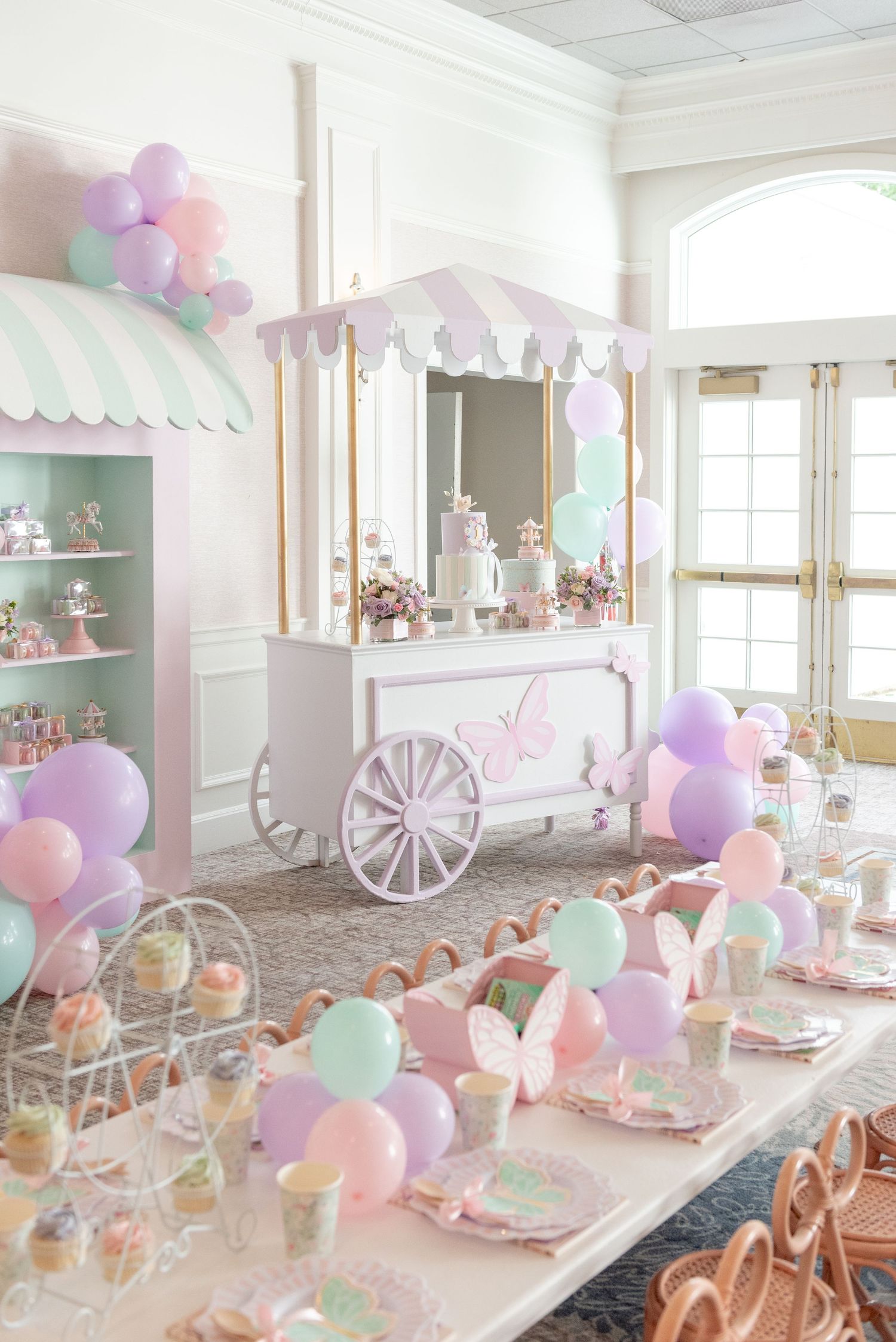 Pastel party room decorated with pink, mint and lavender balloons, featuring elegant table settings and a decorative cart.