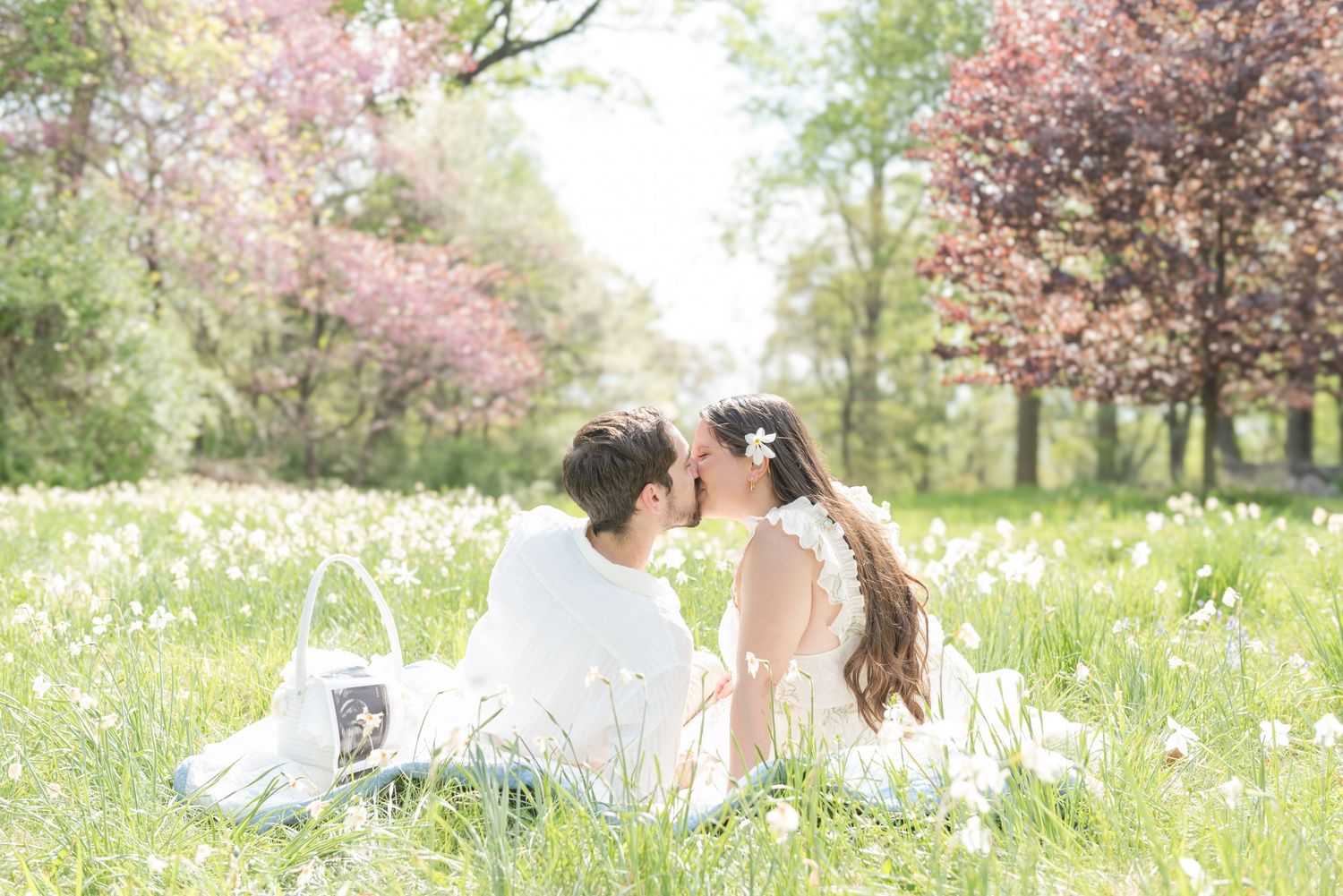 A romantic spring photoshoot in a meadow filled with white wildflowers and blooming cherry trees.