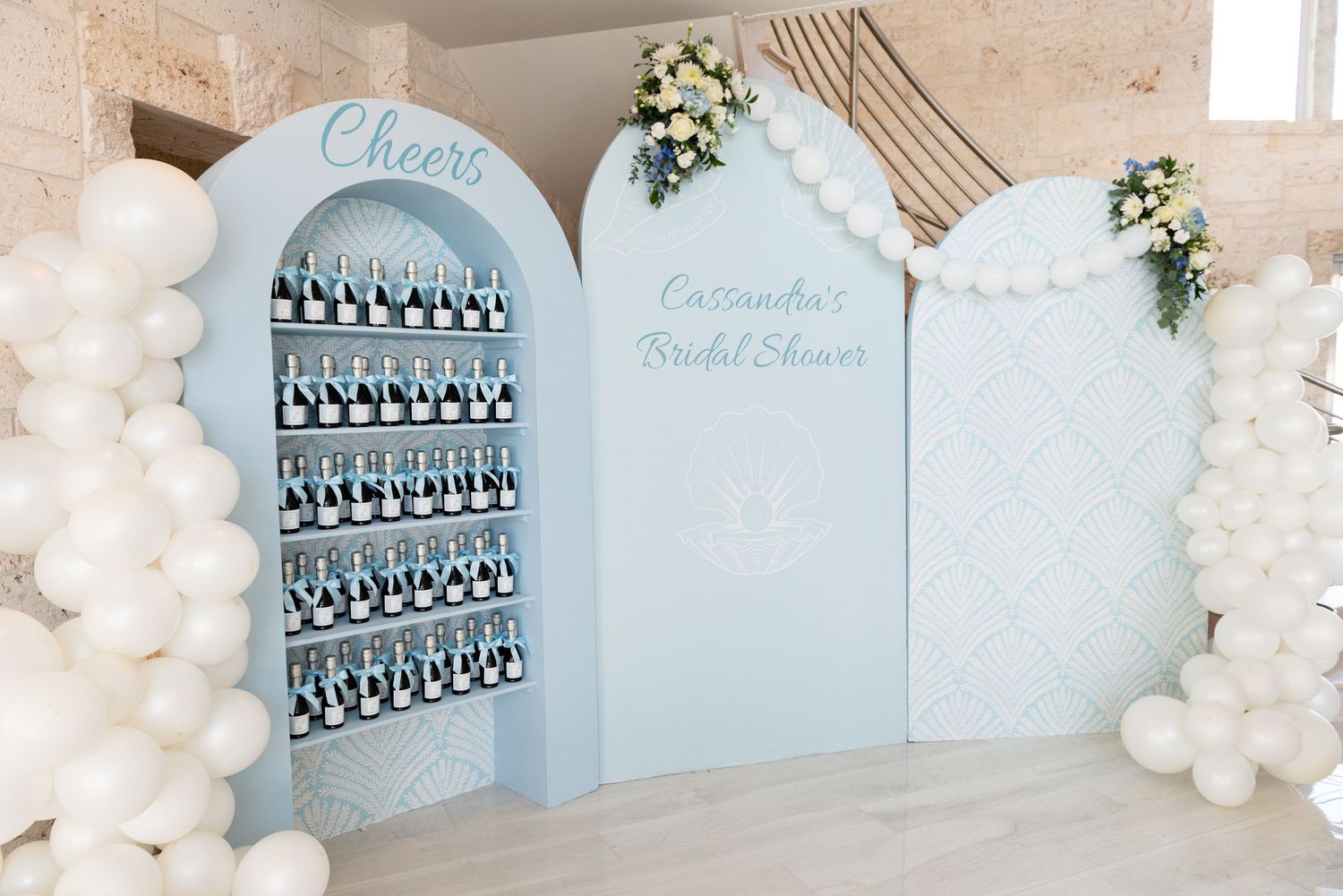 Light blue bridal shower backdrop with balloon garland arch and geometric wall decor in a modern event space.