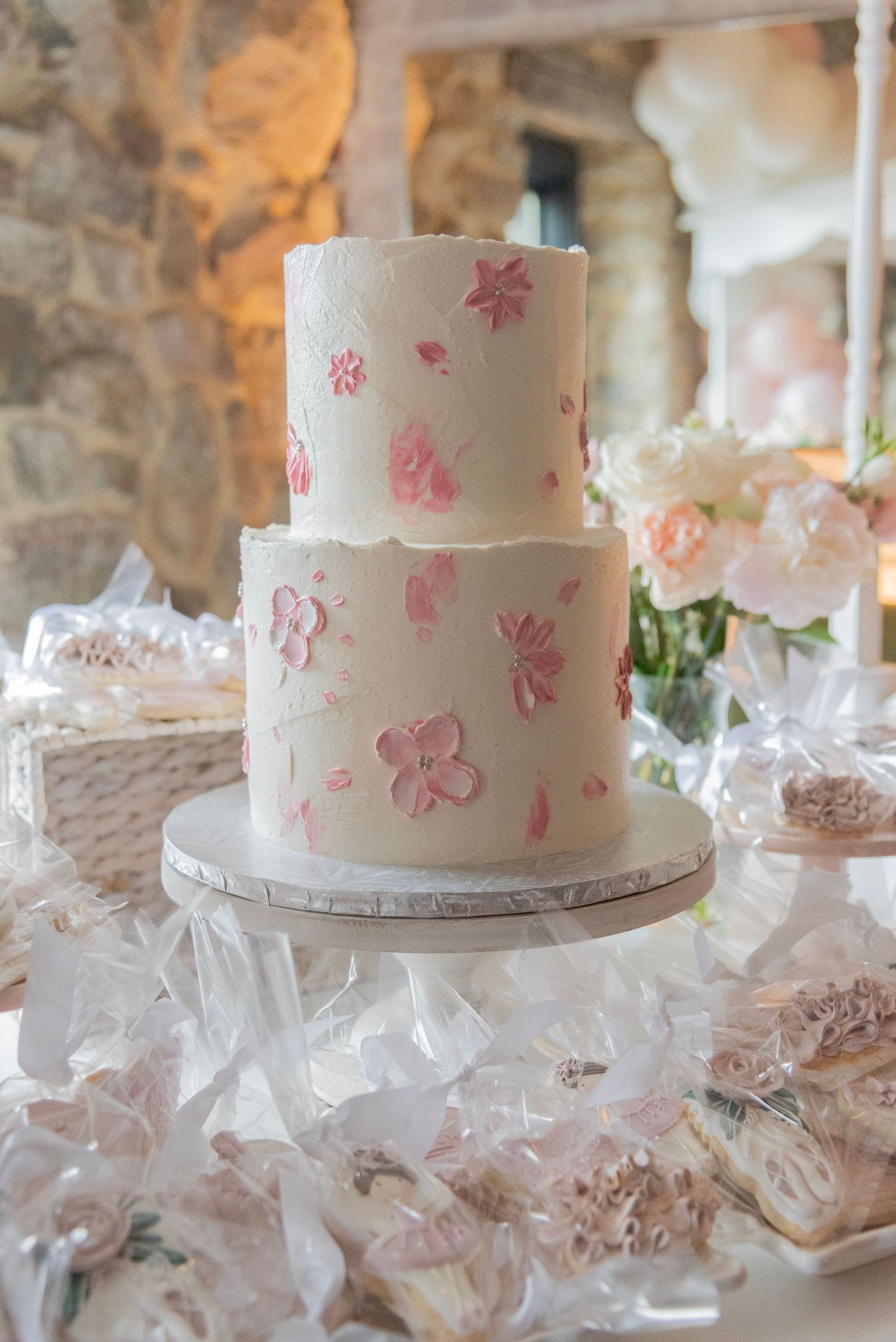 White baby shower cake decorated with delicate pink floral patterns displayed on cake stand with wrapped favors in foreground.