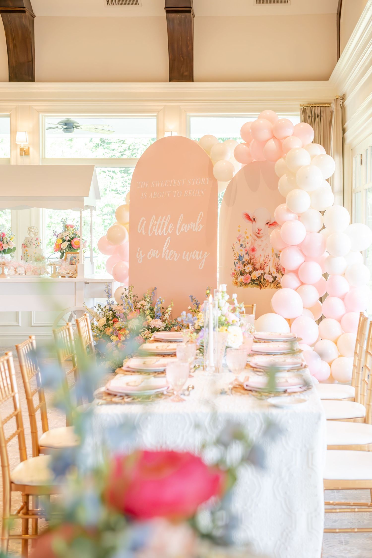 Elegant baby shower table setting with pink balloons, floral arrangements and soft pastel decor in a bright sunlit room.