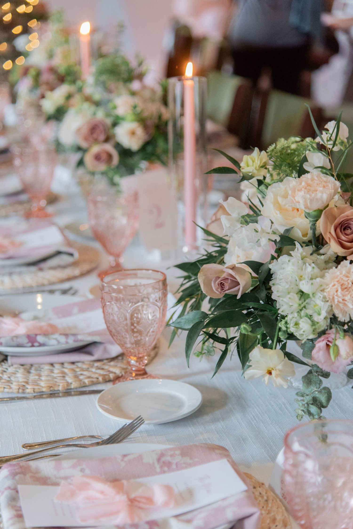 Elegant baby shower table setting with pink glassware, white flowers, and lit taper candles in a romantic atmosphere.