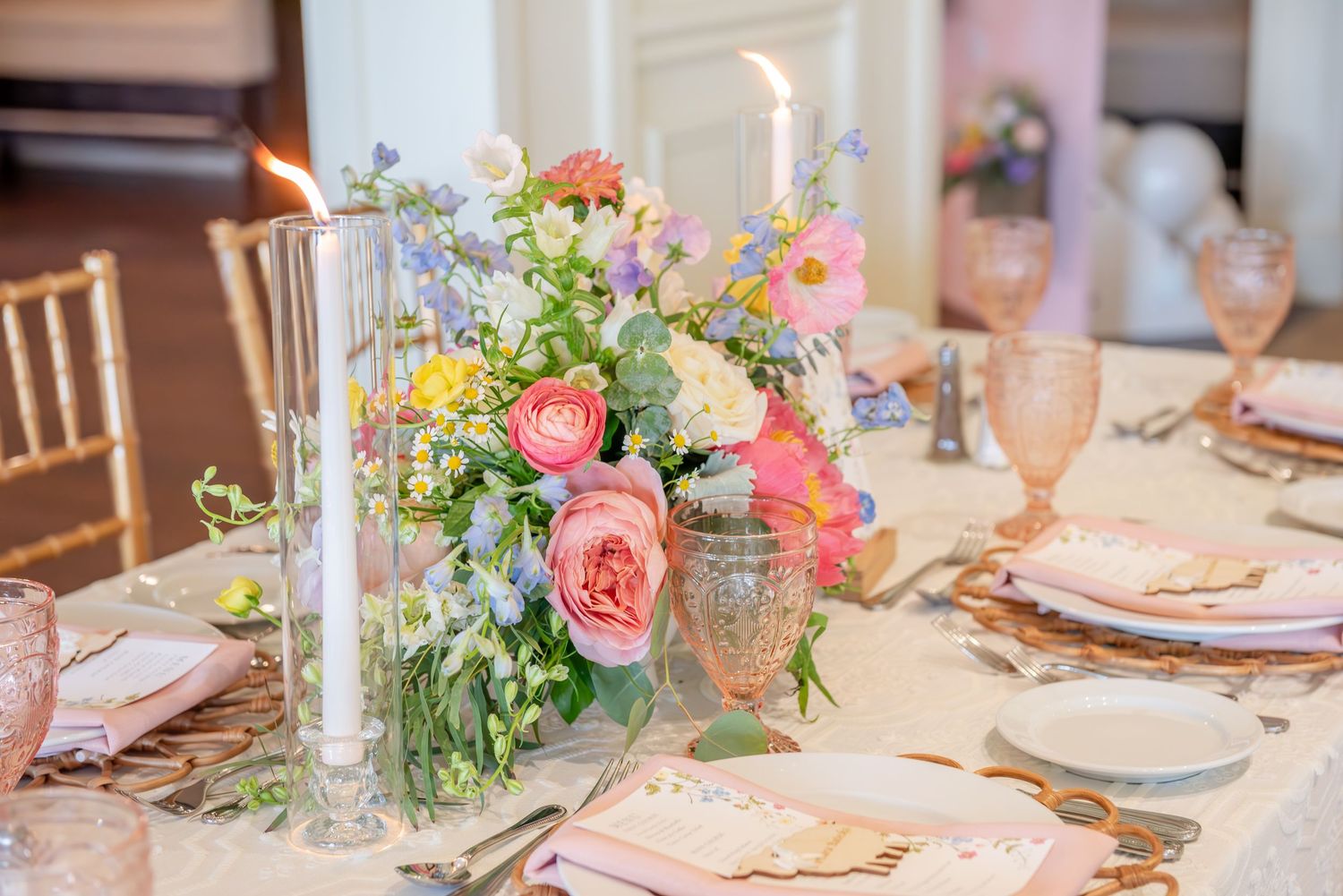Elegant baby shower table with pink floral centerpieces, white candles, and gold accents in a romantic setting.