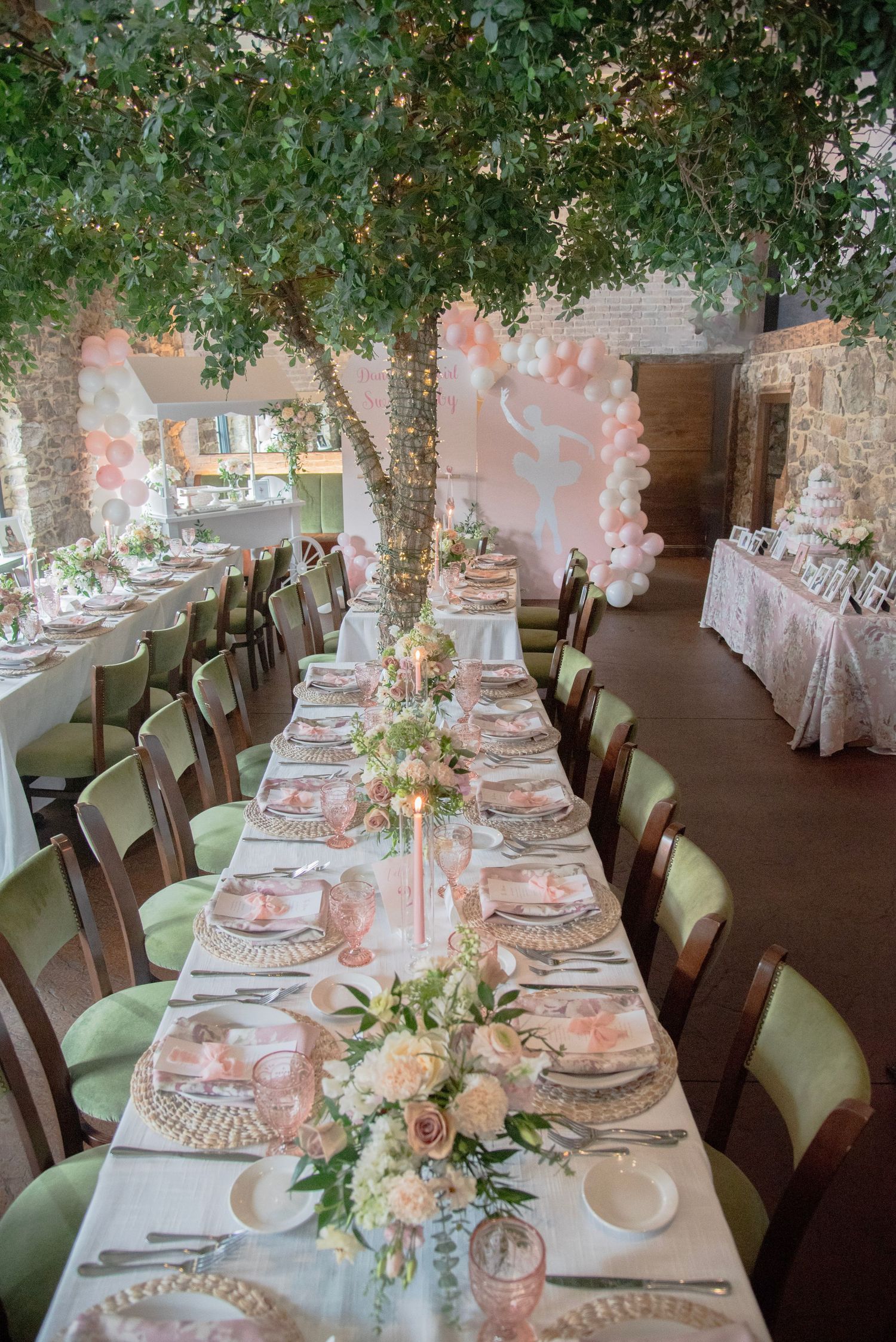 Elegant reception tables decorated with pink and white floral centerpieces under tree branches in a rustic venue.