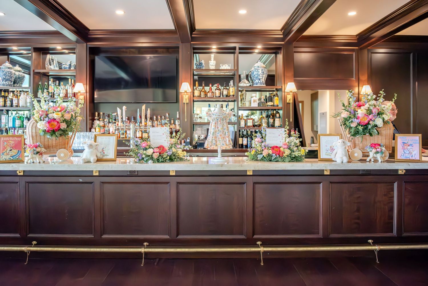 Elegant bar setup with dark wood paneling, floral arrangements, and sweet decor for a baby shower.