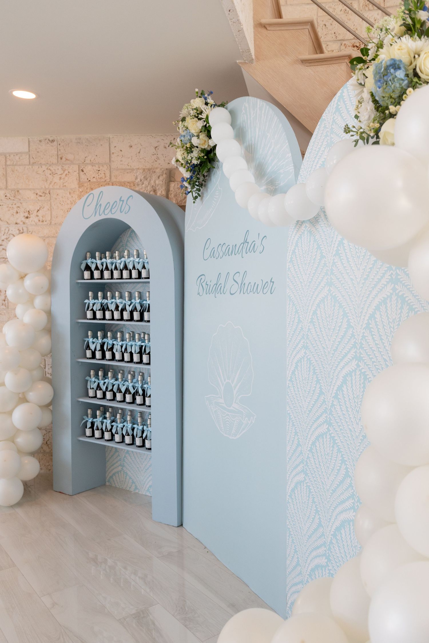 Light blue arched display wall with glass bottles and floral decorations at a bridal shower event.