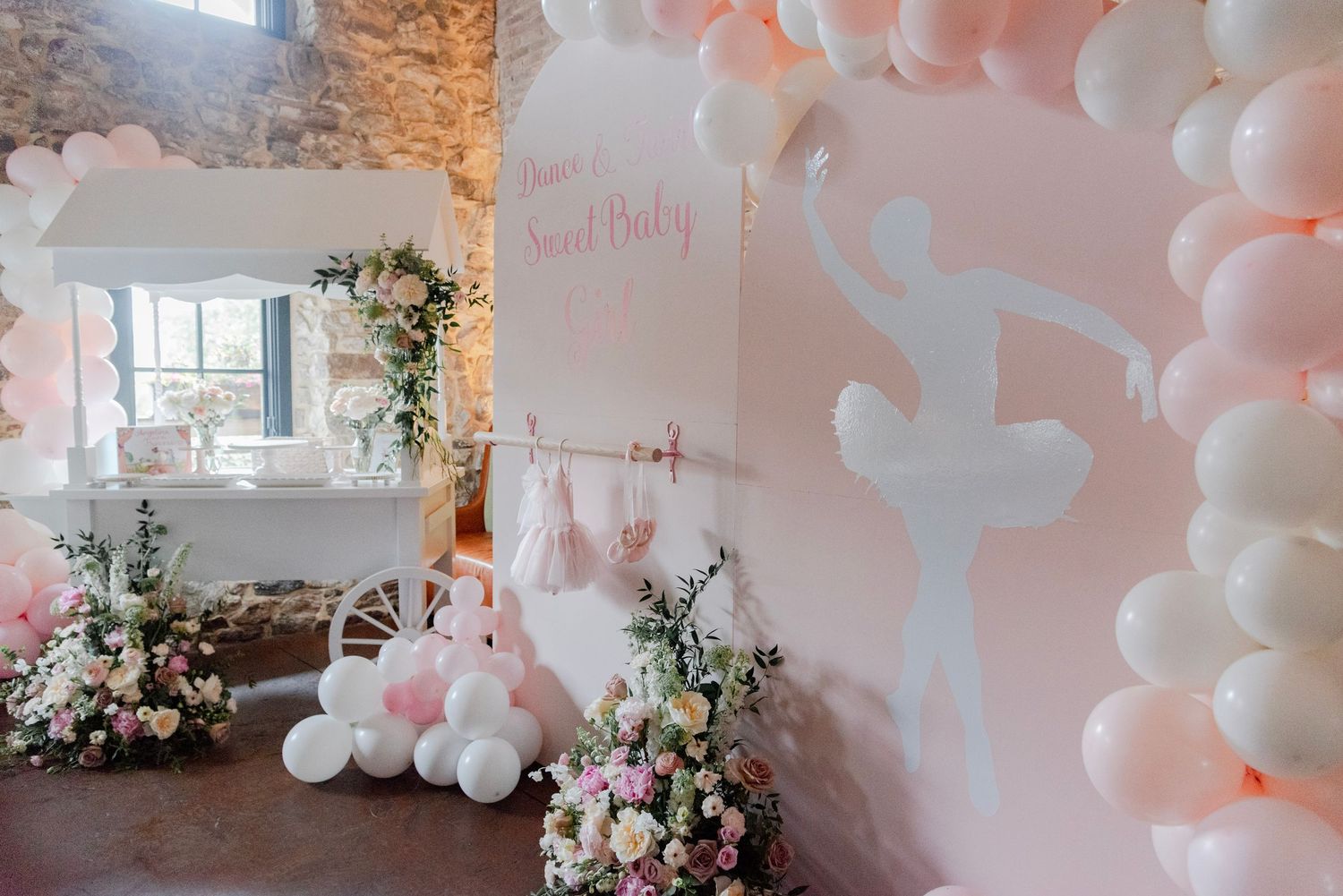Pink and white balloon arch installation with floral arrangements decorates an elegant indoor event space.