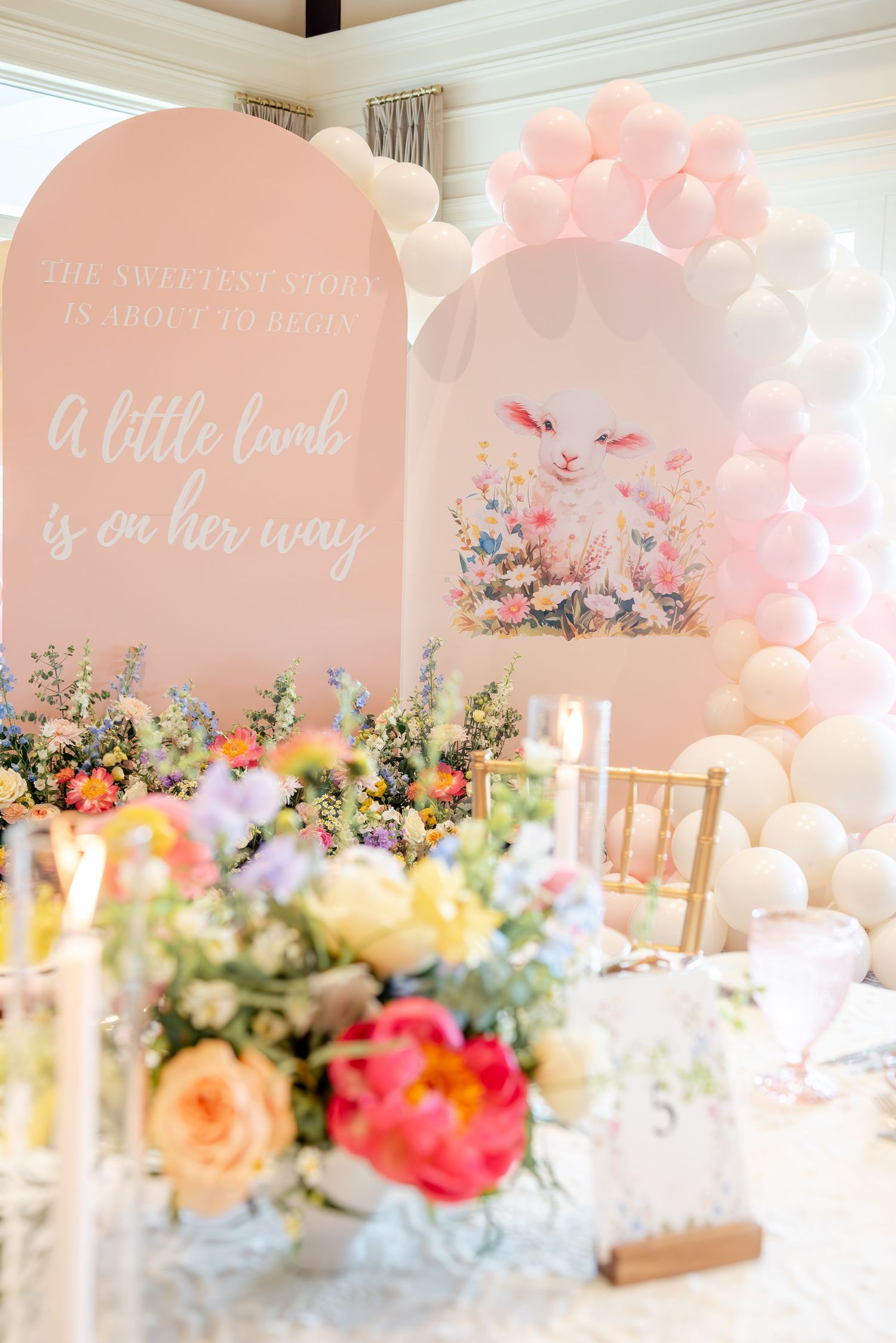 Elegant baby shower decor with pink balloons, floral arrangements and cursive text signs in pastel colors.