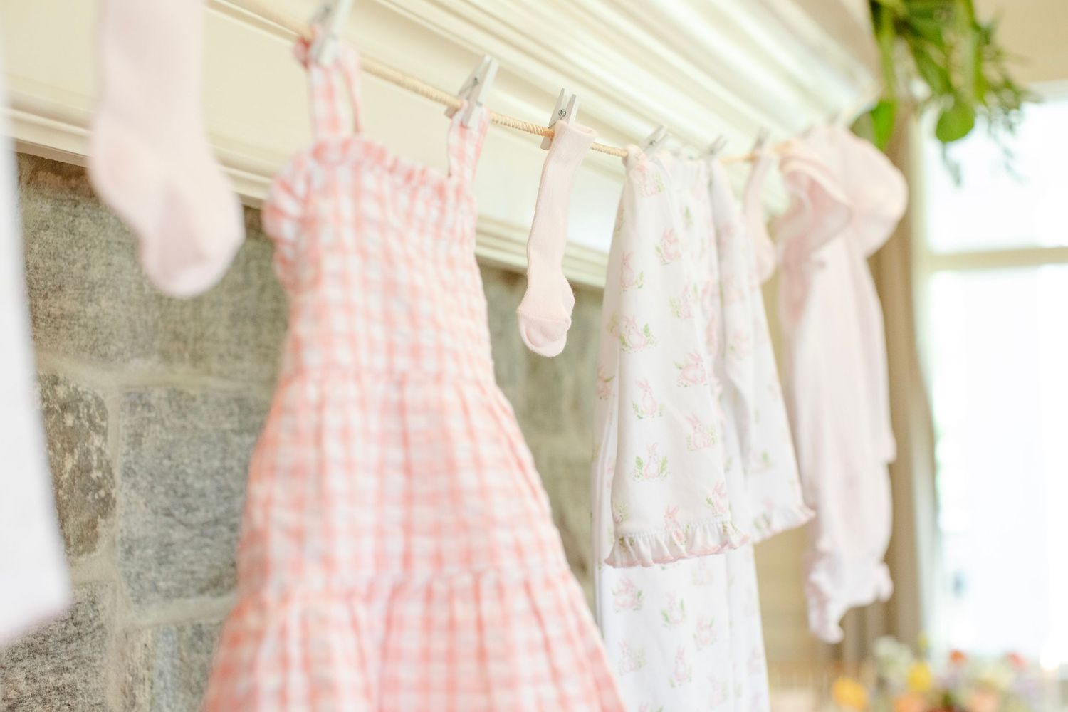 Pink and white gingham dresses and clothing items hang on a rustic clothesline against a light background.