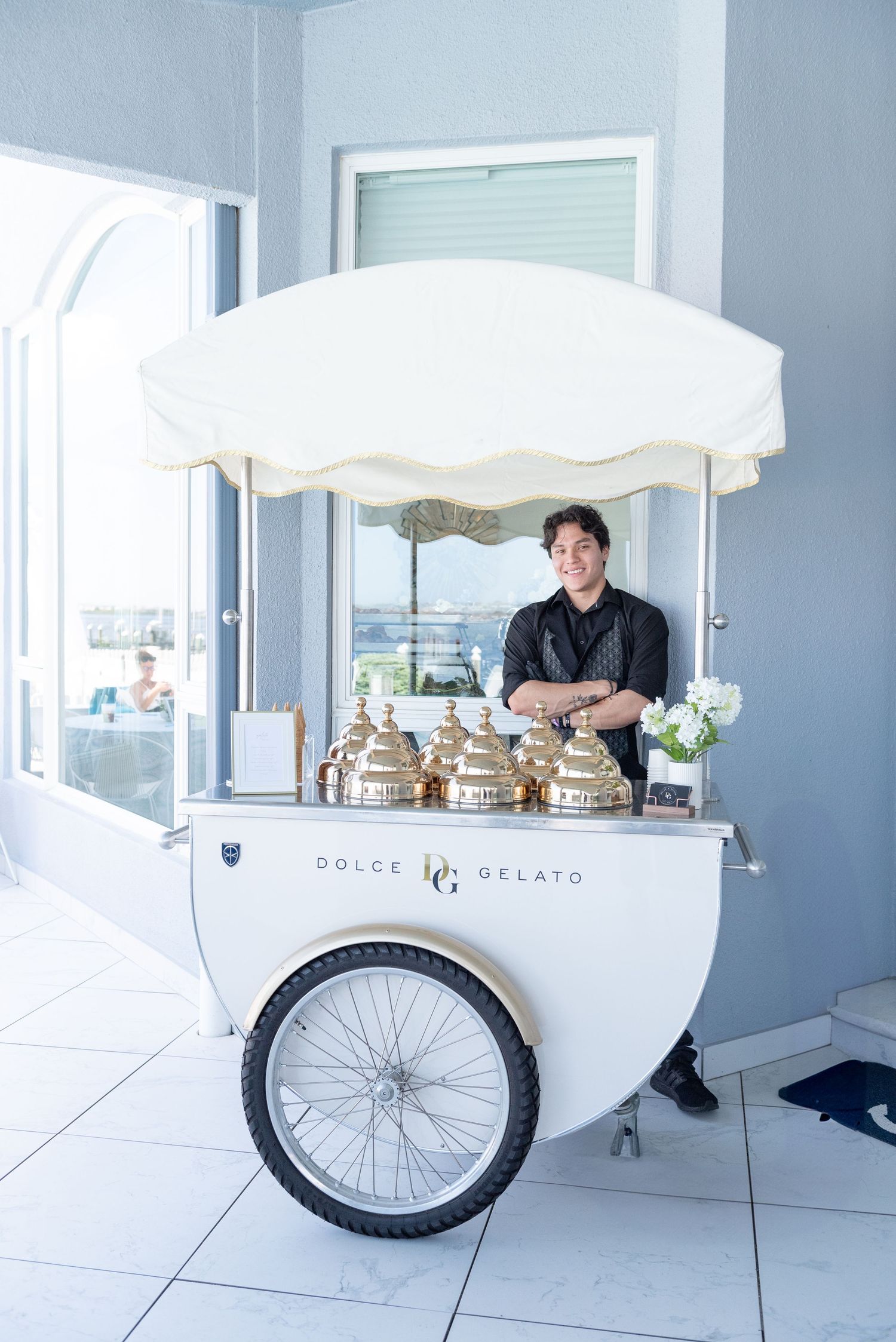White mobile gelato cart with bicycle wheel stands in bright modern space.