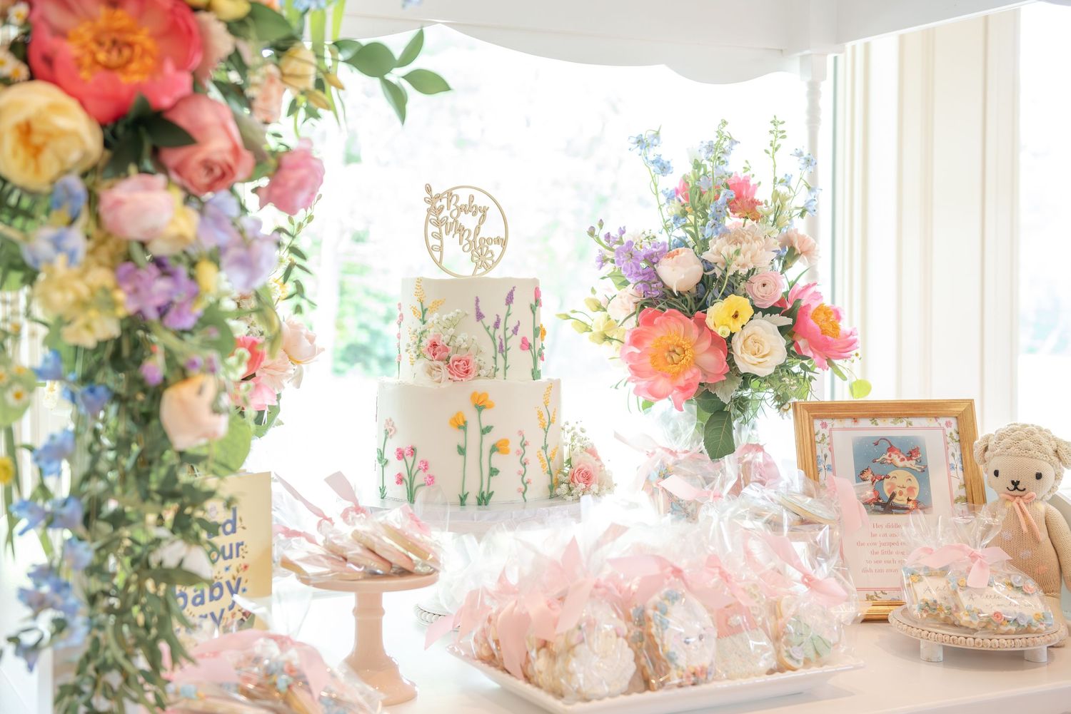 Dessert setup with pink and coral floral arrangements, vintage nursery rhymes, and pastel decorations on a sweet cart.