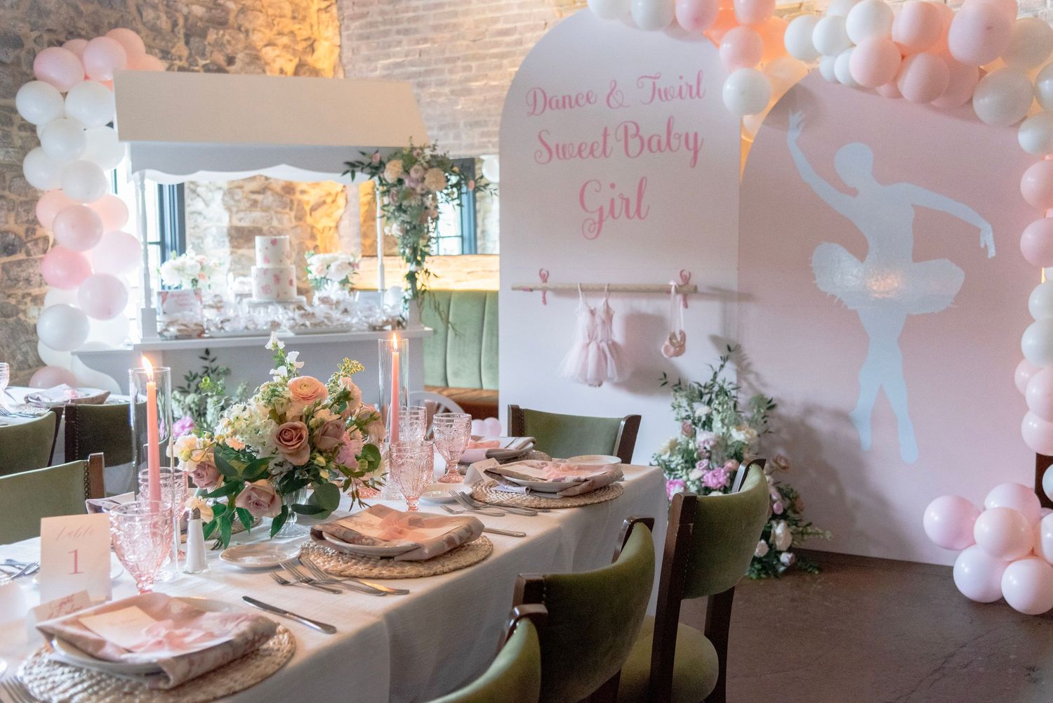 Elegant baby shower table setting with pink balloon arch, floral centerpieces and 'Sweet Baby Girl' signage in pastel decor.