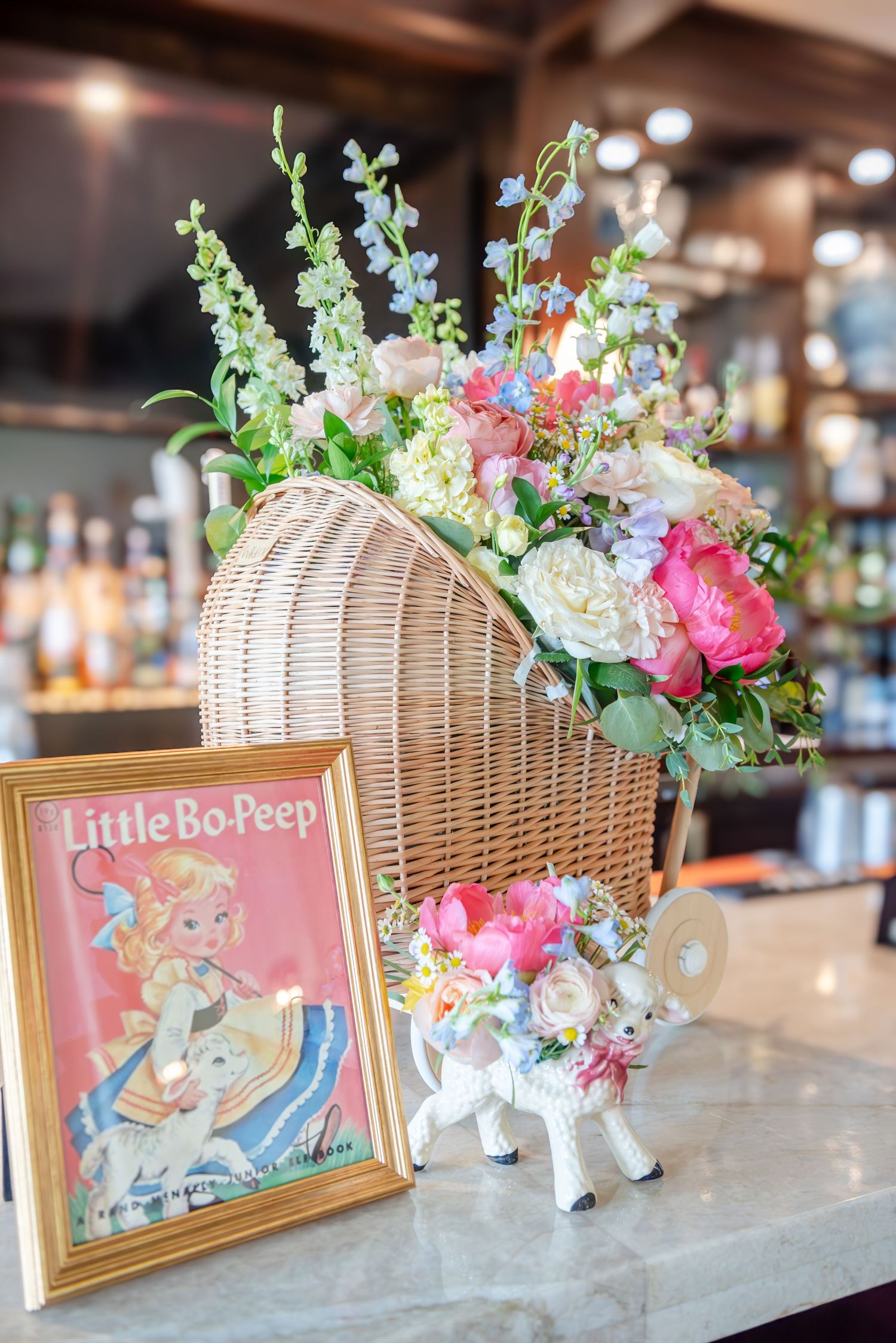 Vintage Little Bo Peep storybook frames paired with wicker baskets filled with pink and white floral arrangements on a counter.