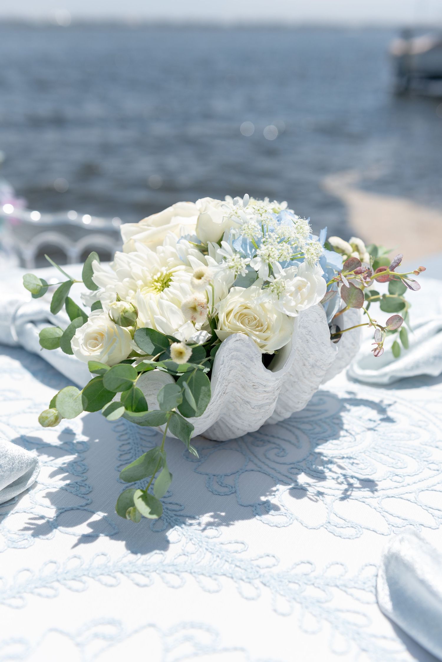 White floral centerpiece with roses and greenery arranged elegantly on a light tablecloth at a seaside wedding reception.