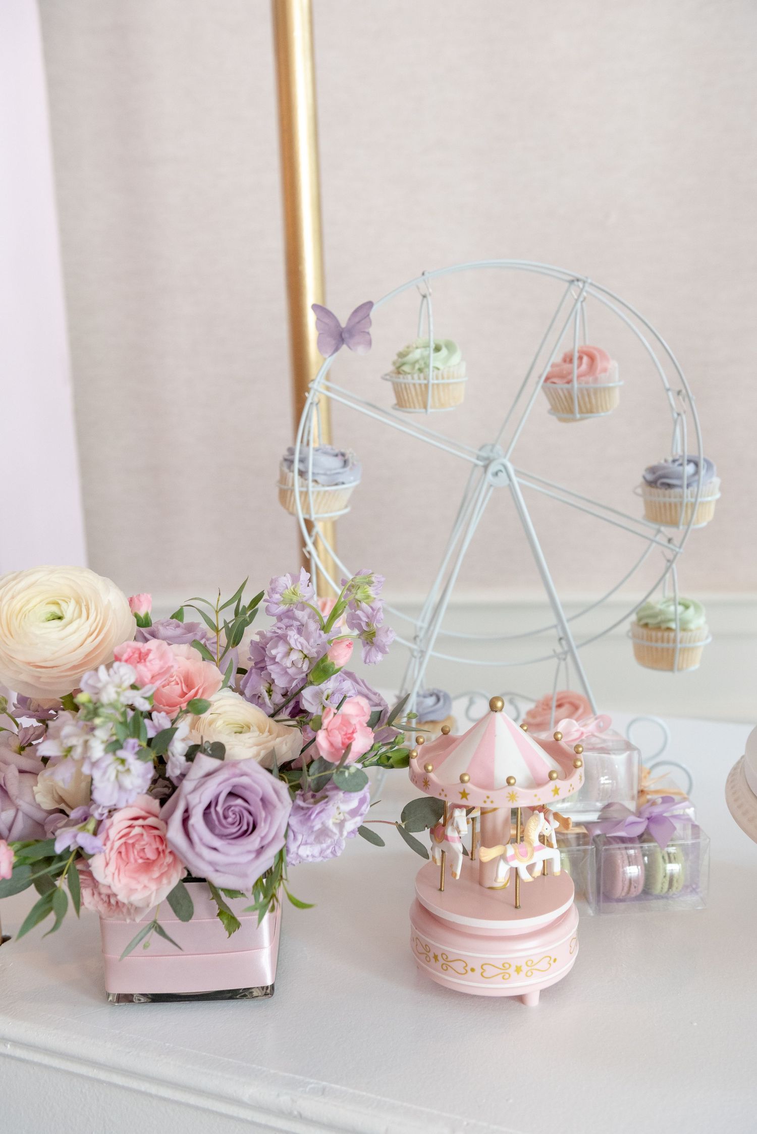 Pastel party decor featuring a miniature Ferris wheel, pink carousel music box, and elegant floral arrangement with roses.
