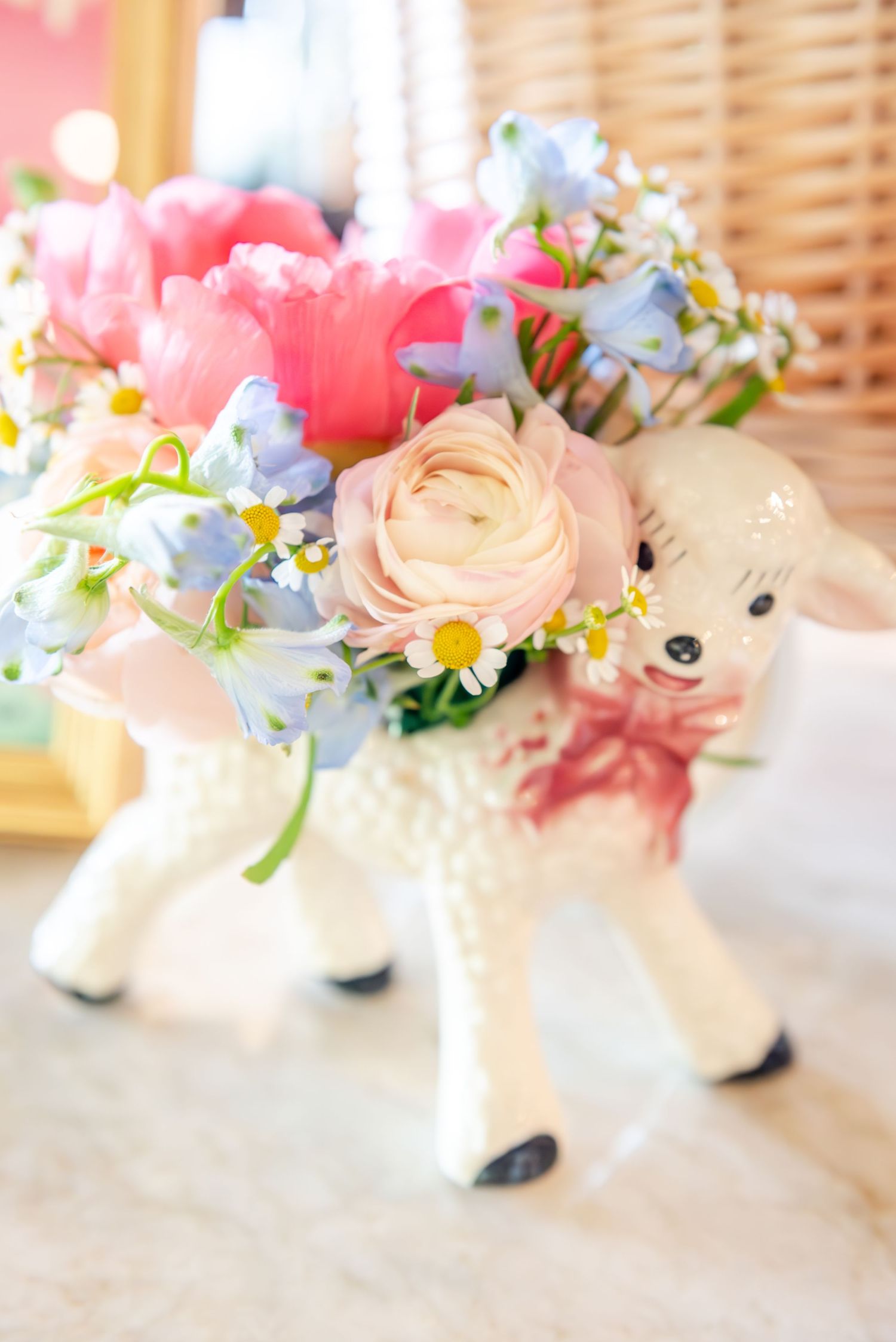 A charming ceramic lamb vase filled with pink ranunculus, blue forget-me-nots and spring flowers in a soft pastel arrangement.