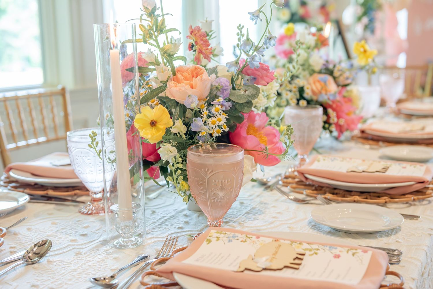 Elegant table settings with peach and coral floral centerpieces arranged in a row for a baby shower.