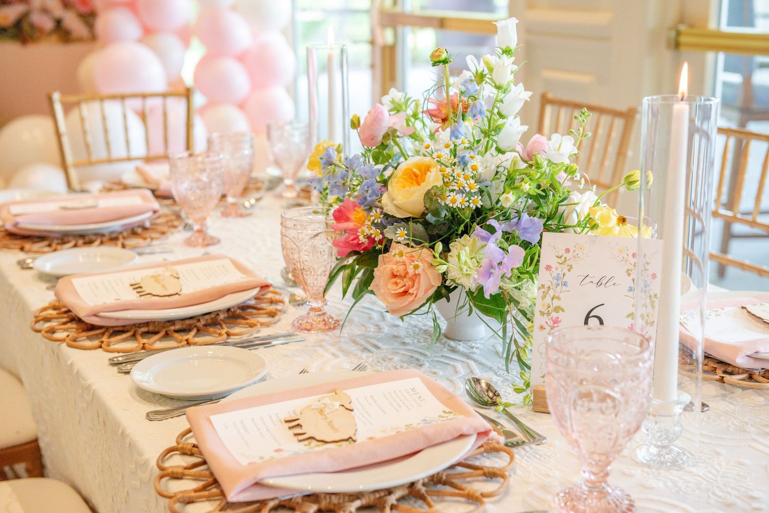 Elegant table settings with pink and peach floral centerpieces and gold charger plates in a bright dining room.