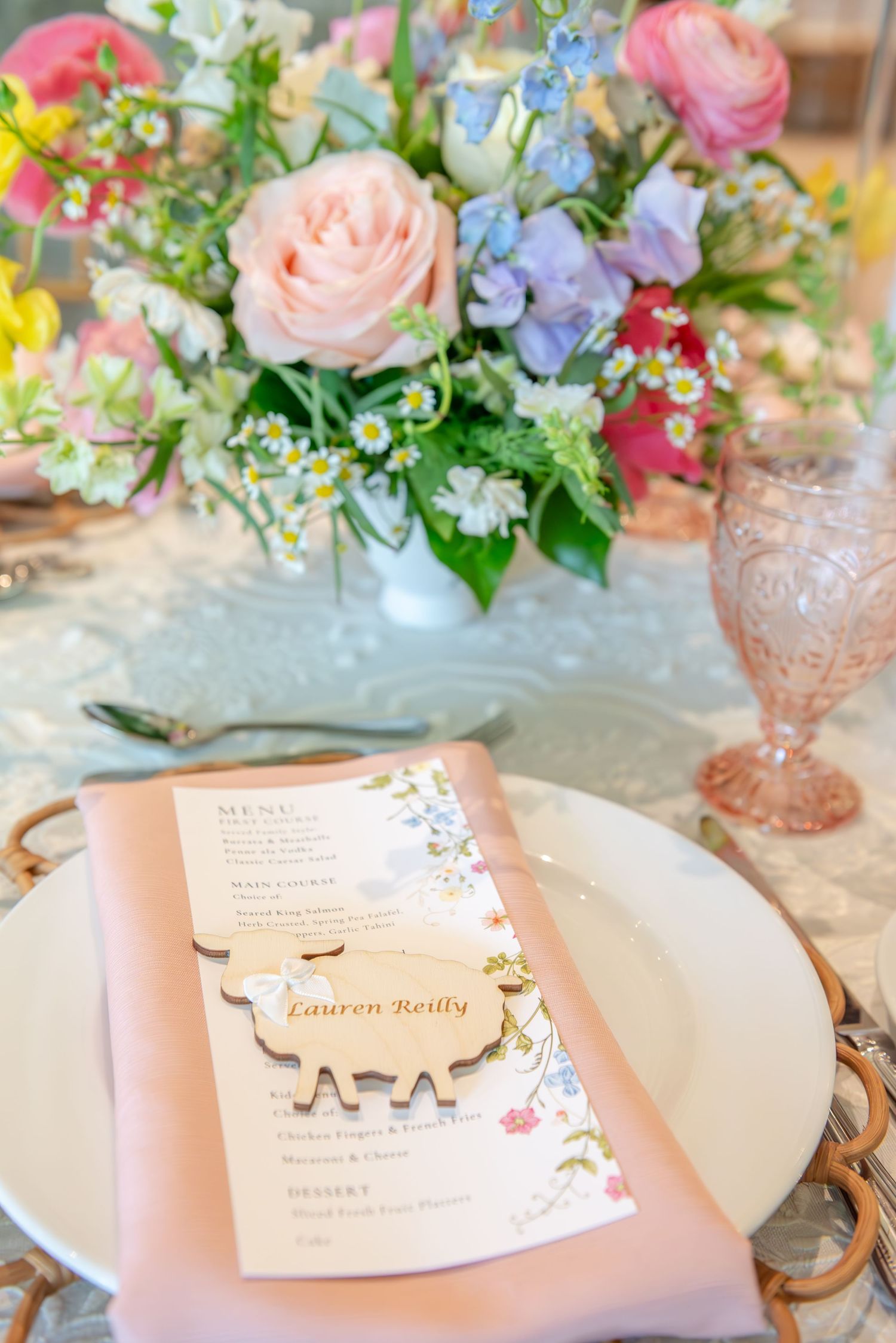 Pink floral centerpieces and place settings with delicate menu cards create an elegant table arrangement for a special event.