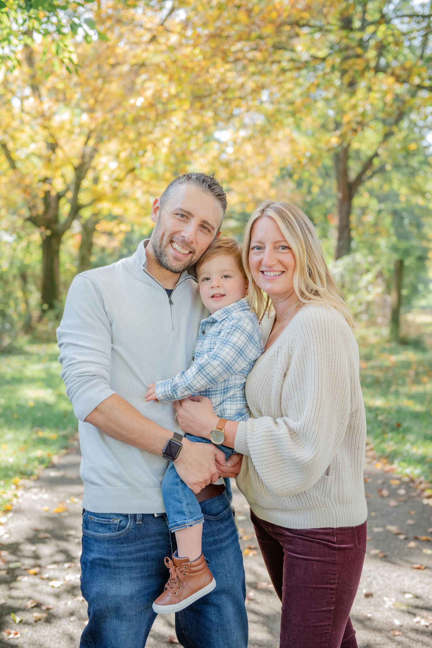 A family shares joyful moments together in a park with golden autumn foliage in the background.