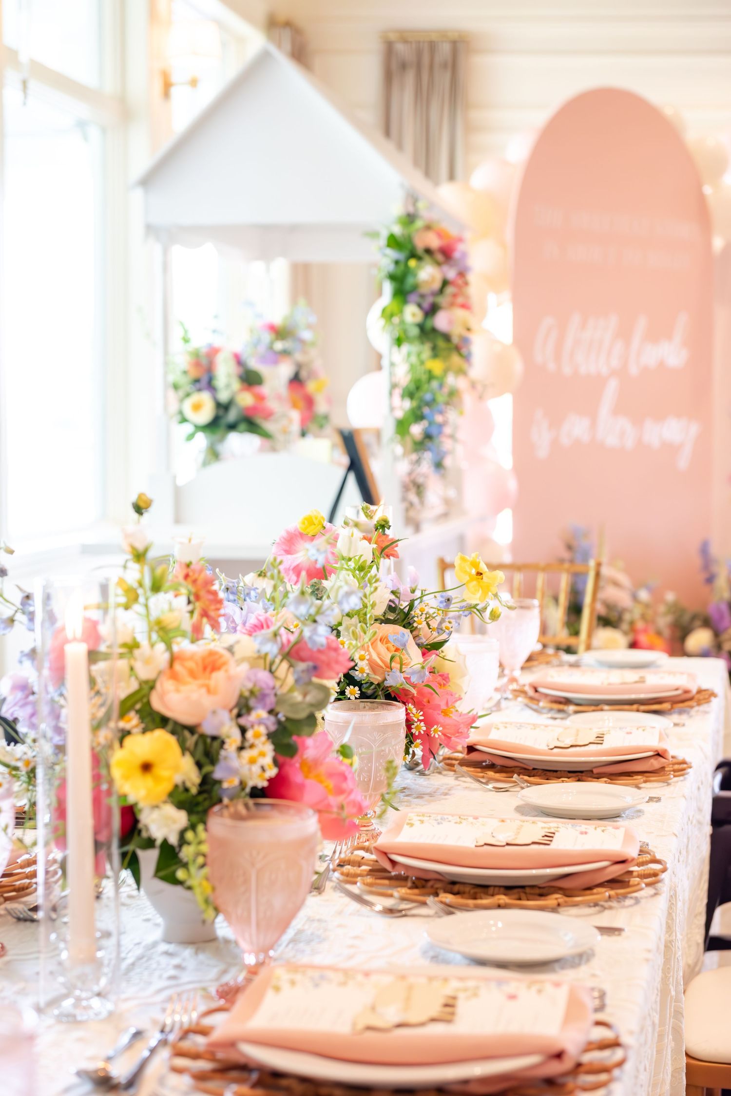 Elegant table settings with pink and peach tones feature floral centerpieces and white place settings at a baby shower.