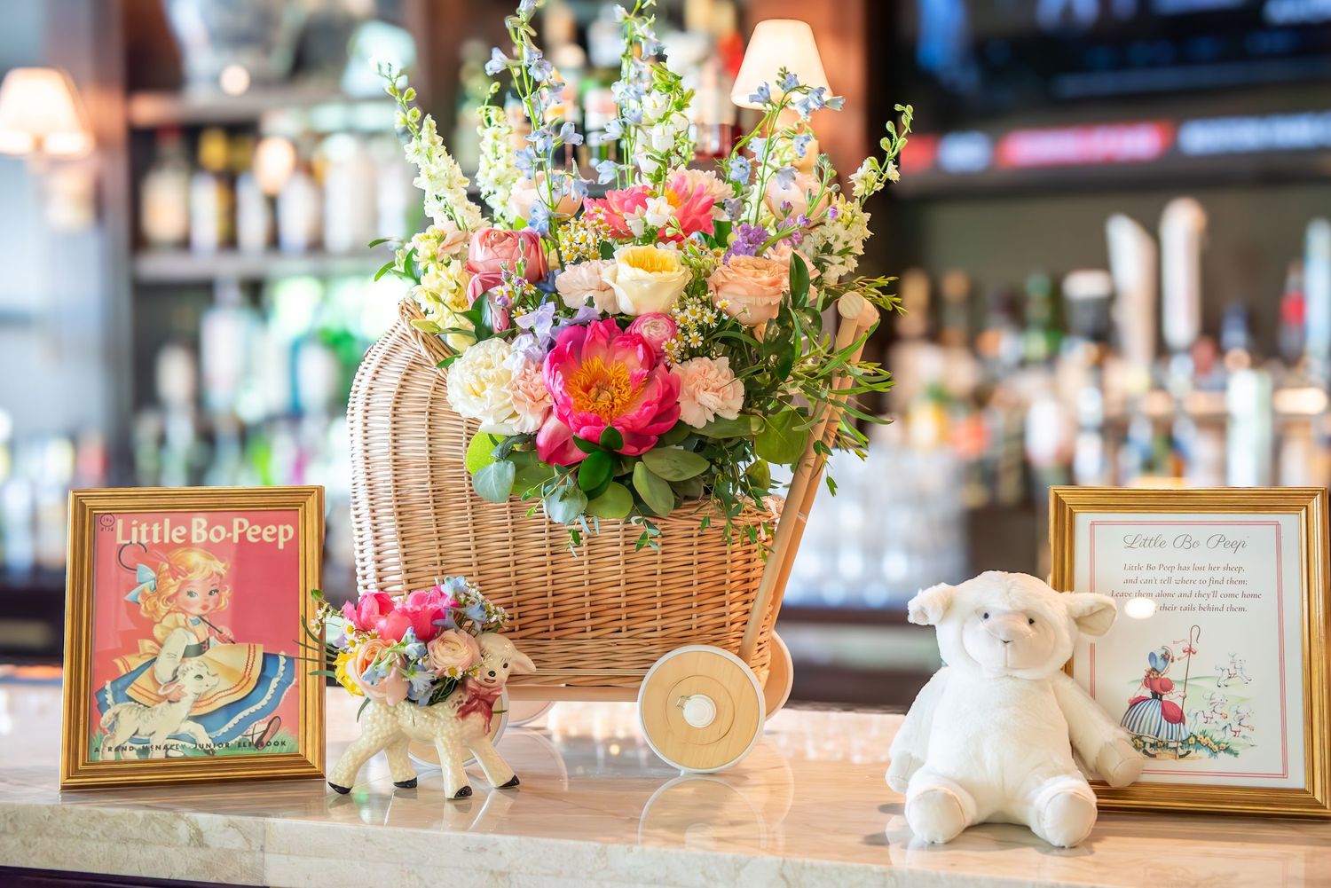 Nursery rhyme baby shower decor features colorful floral arrangements and framed photos displayed along a bar.