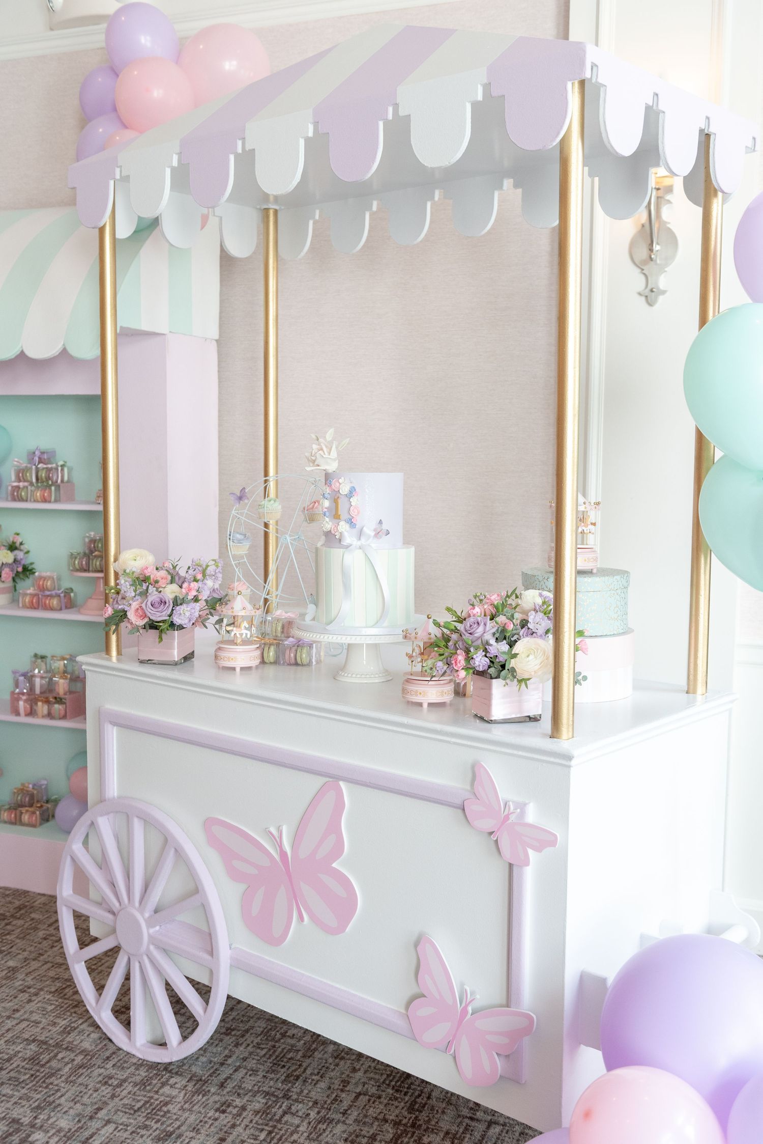 A pastel pink and white candy cart display with butterflies and balloons in soft mint and lavender colors.