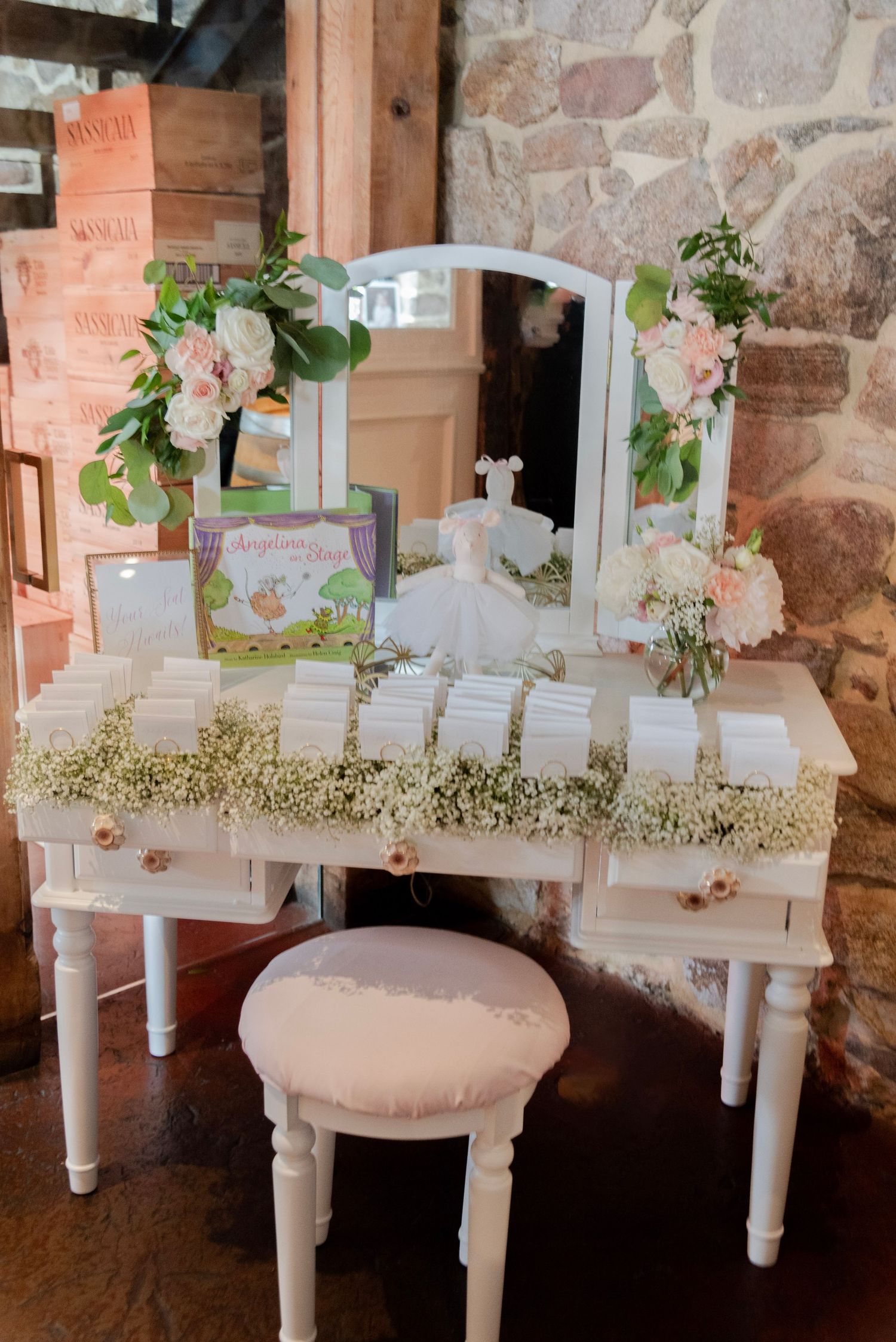 White vintage vanity decorated with baby's breath flowers and escort cards creates an elegant display against stone wall.