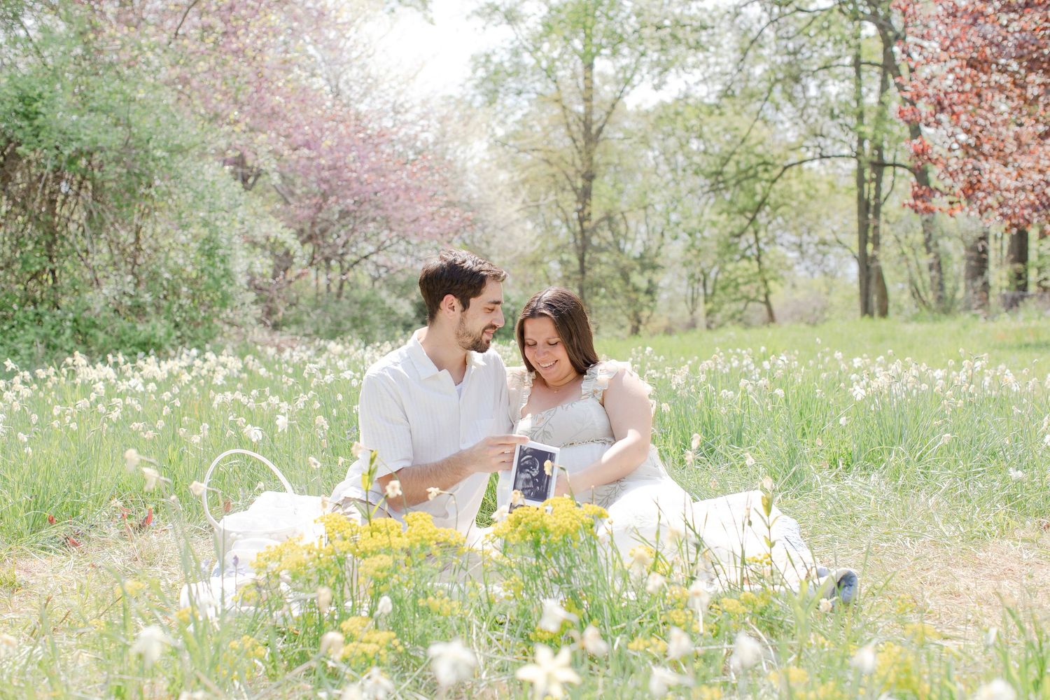 A couple enjoys a romantic spring picnic surrounded by blooming cherry trees and scattered yellow flowers in a serene garden.