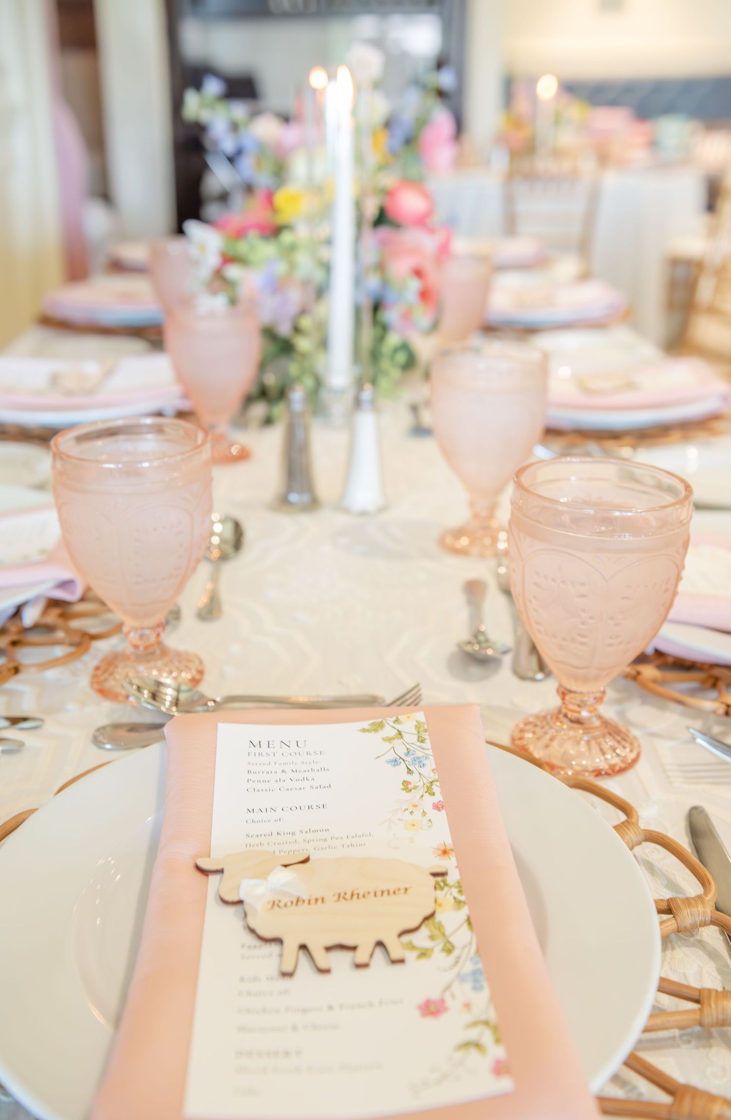 Elegant table setting with pink glassware, floral centerpieces, and delicate menu cards on white plates.