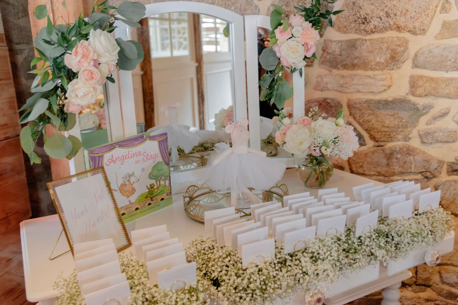 Elegant seating chart display with white floral arrangements and greenery against a rustic stone wall.