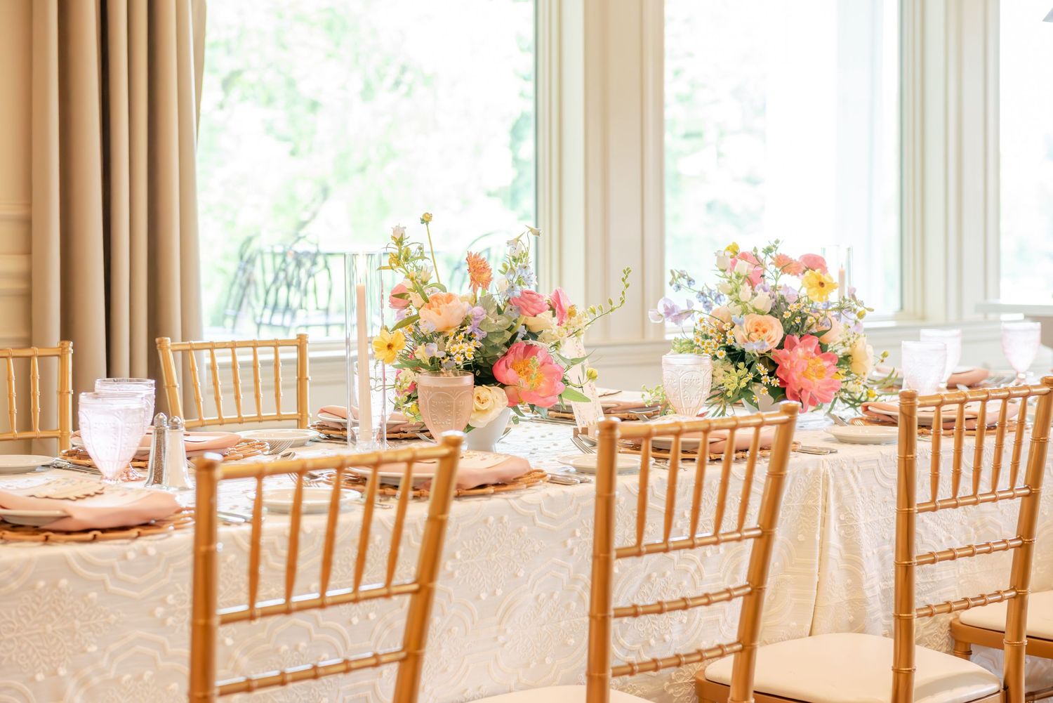 Baby Shower tables with gold chiavari chairs and pink floral centerpieces in a bright sunlit room.
