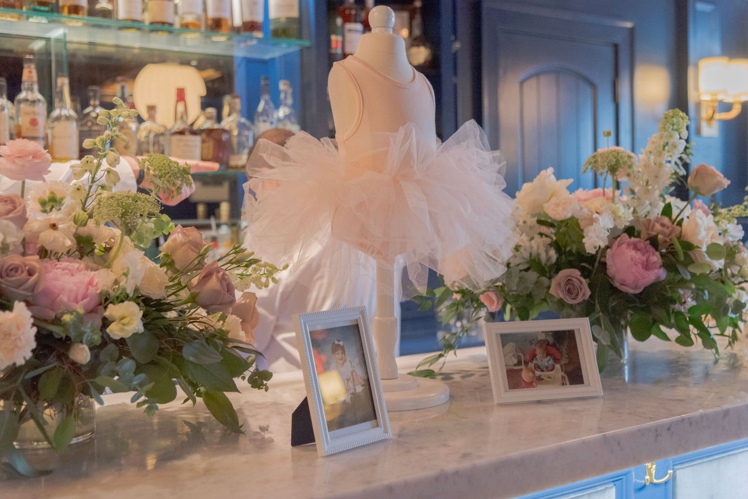 Elegant ballet tutu centerpiece surrounded by pink floral arrangements and framed photos at a special event display.