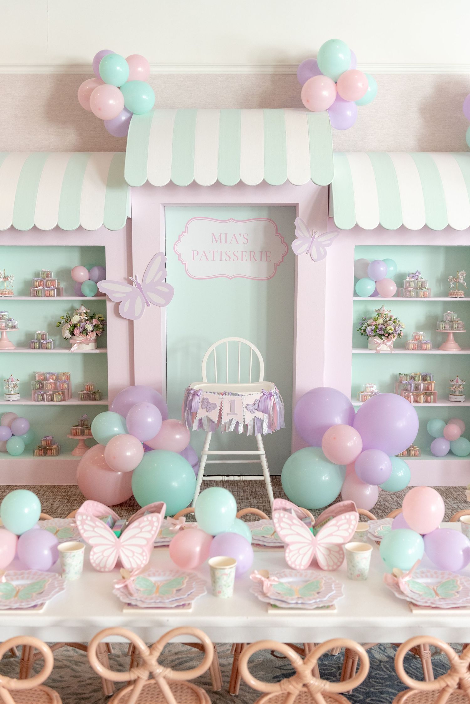 Pastel pink and mint green party setup with balloons, butterflies and scalloped decorations on shelves and tables.