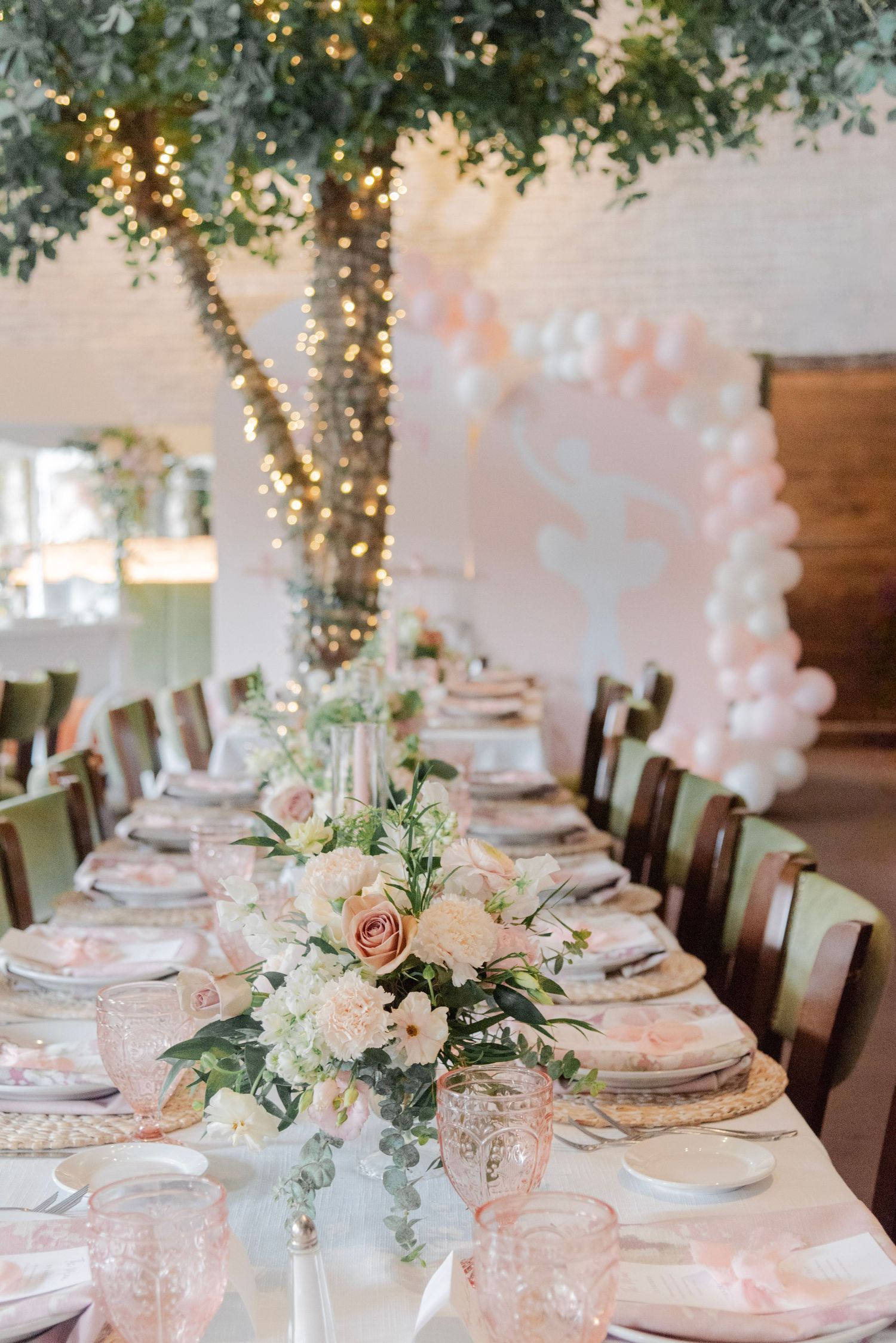 Elegant baby shower table settings with blush pink decor, twinkle lights, and floral centerpieces in a rustic venue.