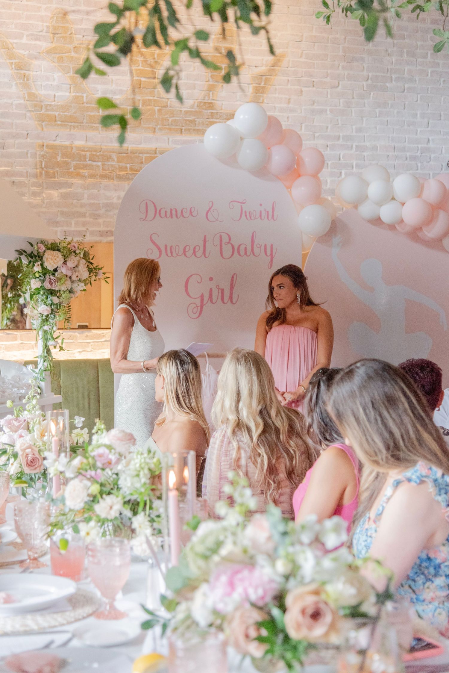 Pink baby shower celebration with balloon arch and floral decorations at an elegant indoor venue.