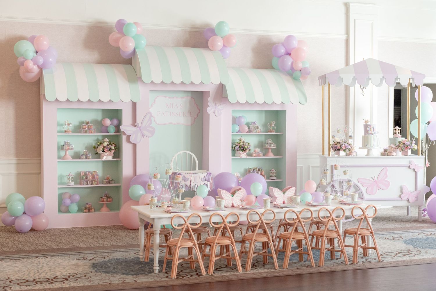 A pastel pink party room decorated with balloons and flowers features elegant table settings and display shelves.