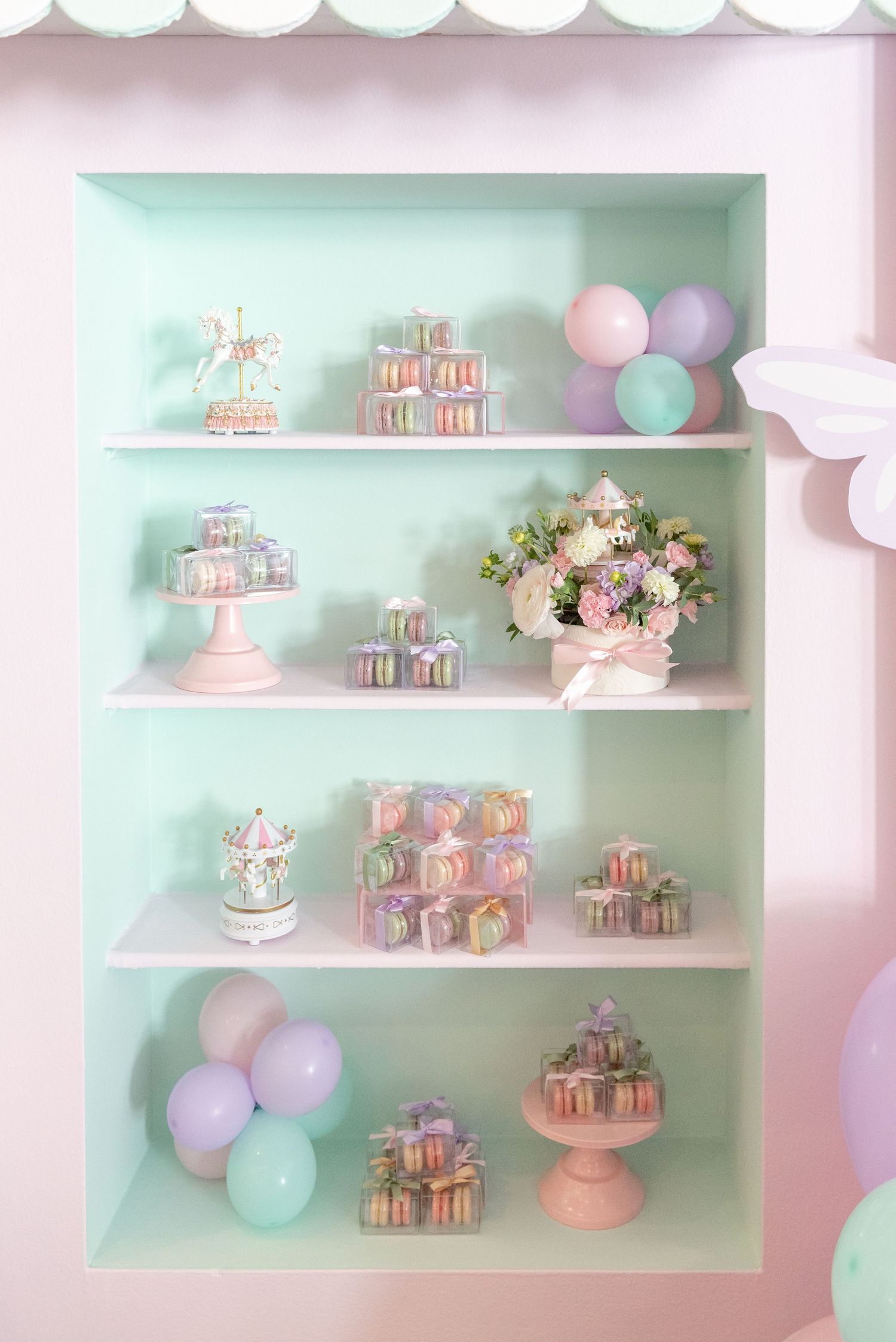 Pastel pink and mint green party display with tiered shelves holding macarons and decorative balloons against soft lighting.