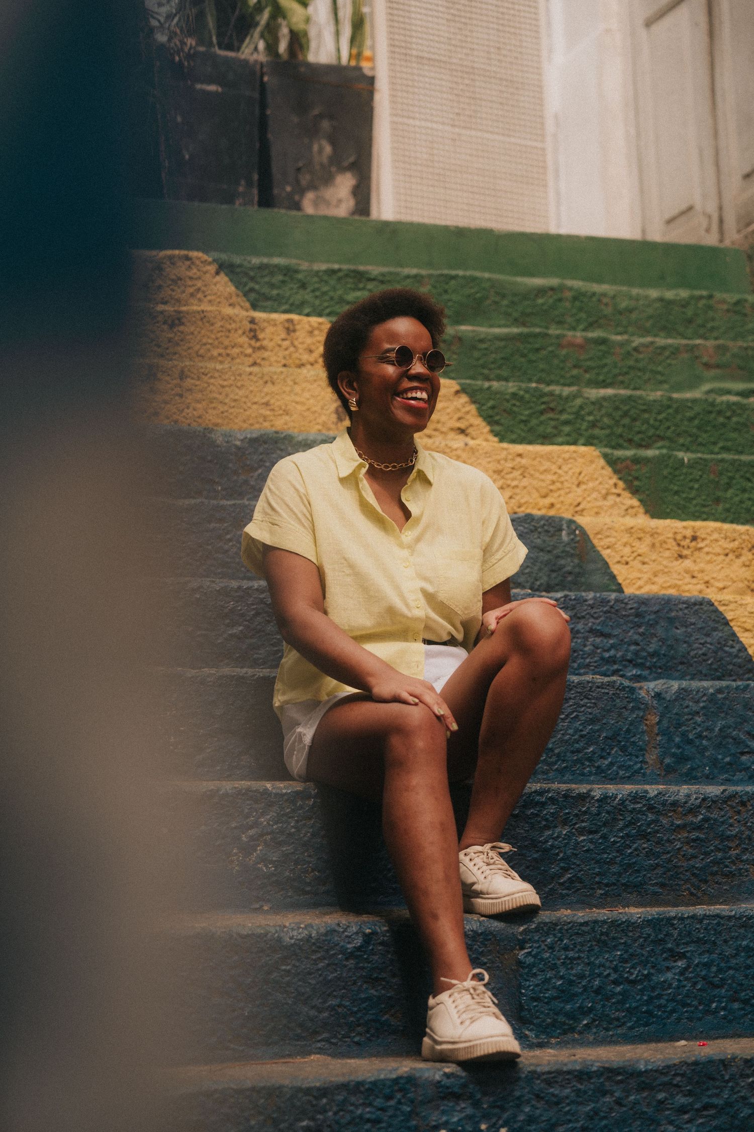 Sequence of someone wearing yellow shirt and white sneakers sitting on painted concrete steps in sunlit outdoor setting.