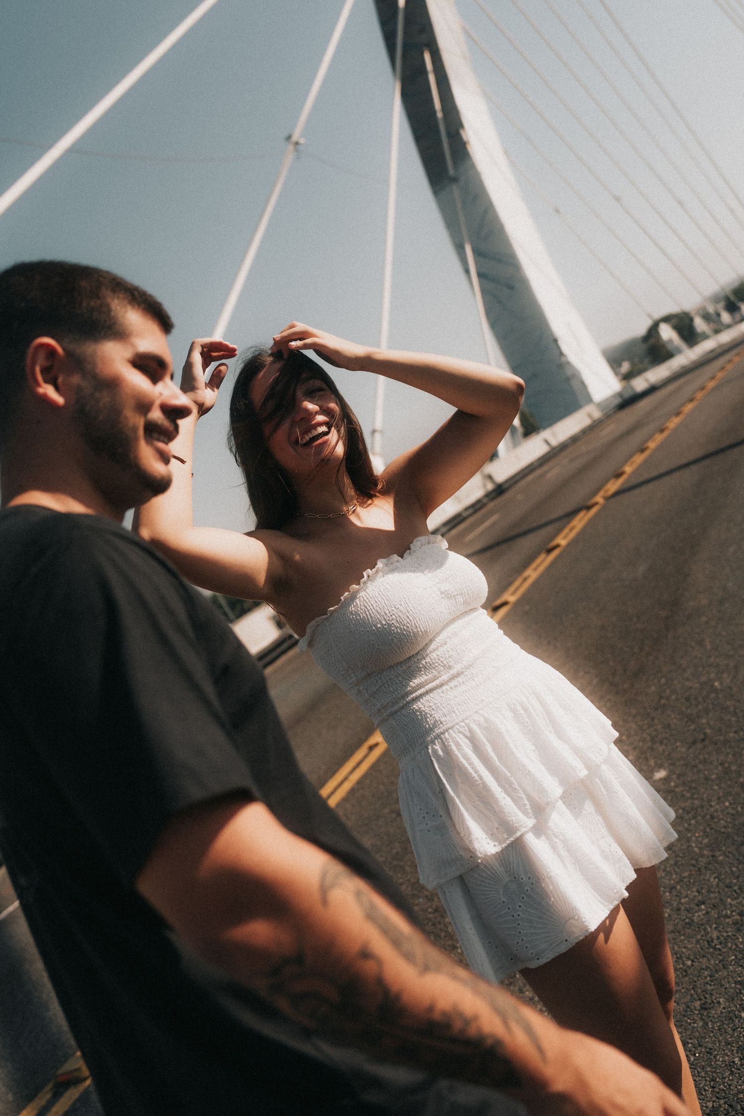 Happy couple embraces on a bridge during sunset creating candid silhouettes against bright sky.