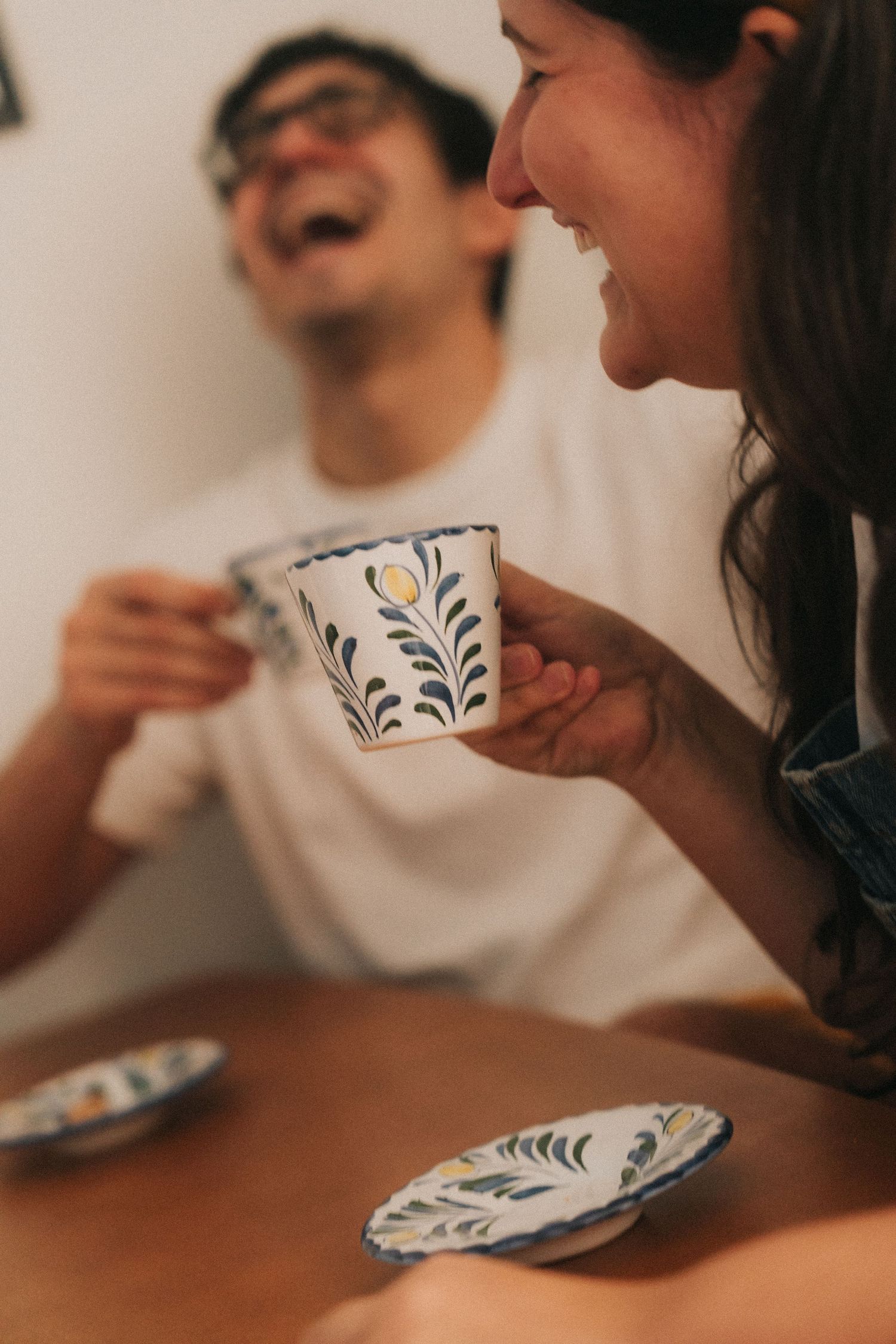 Multiple cups with blue floral patterns rest on a wooden surface as people enjoy drinks and conversation together.