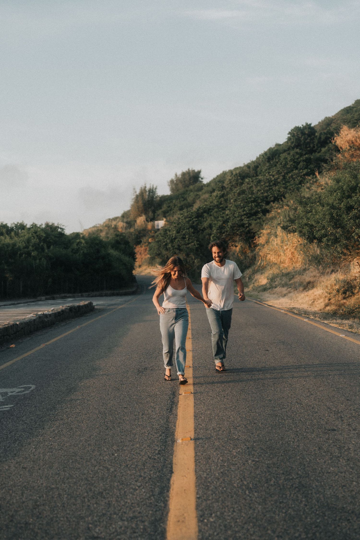 Two people walking together down an empty mountain road during golden hour.