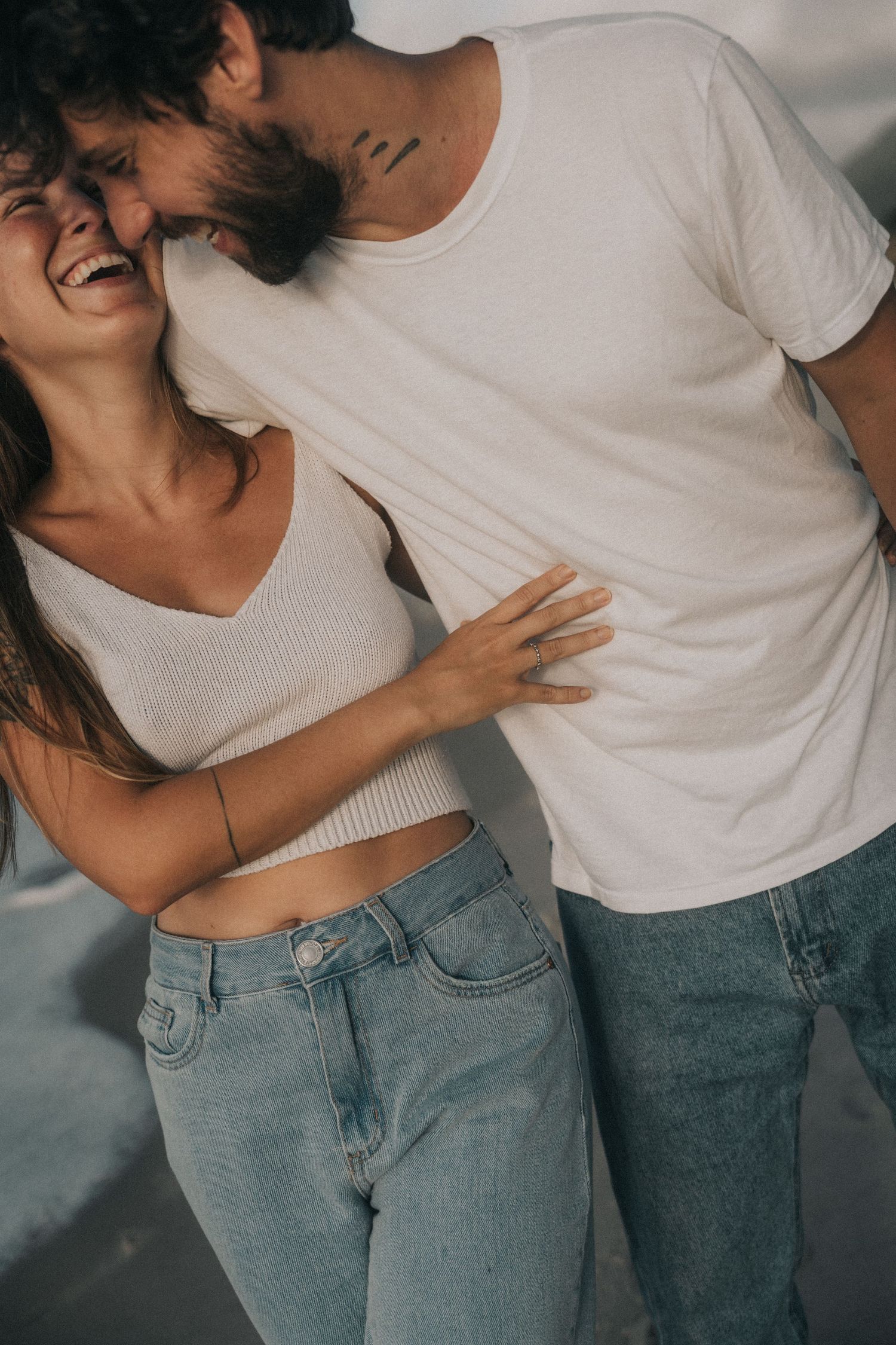 A couple wearing white tops and light denim jeans share intimate and playful moments in a series of casual poses.