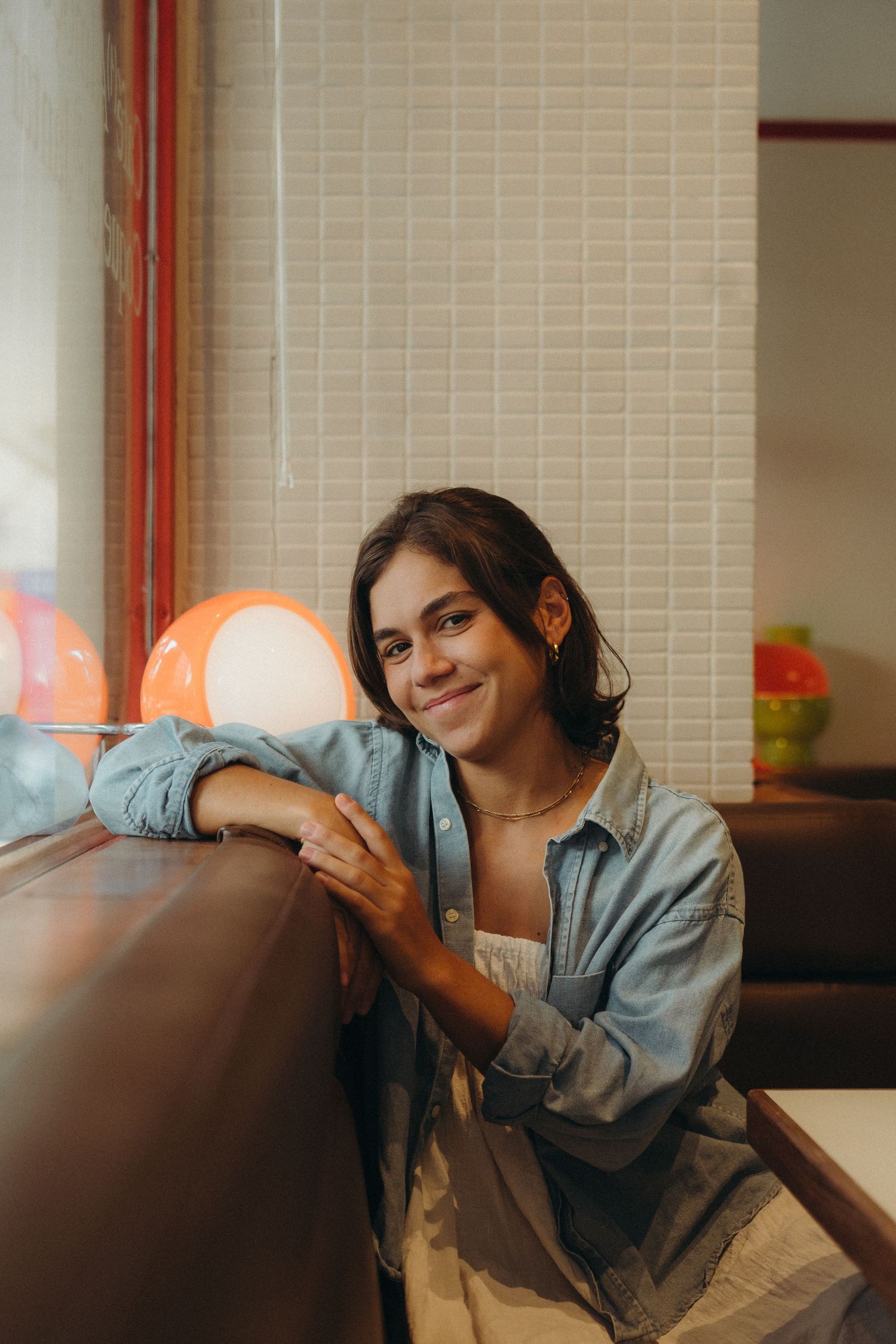 A casual portrait showing someone relaxing at a cafe table wearing a denim shirt and white top.