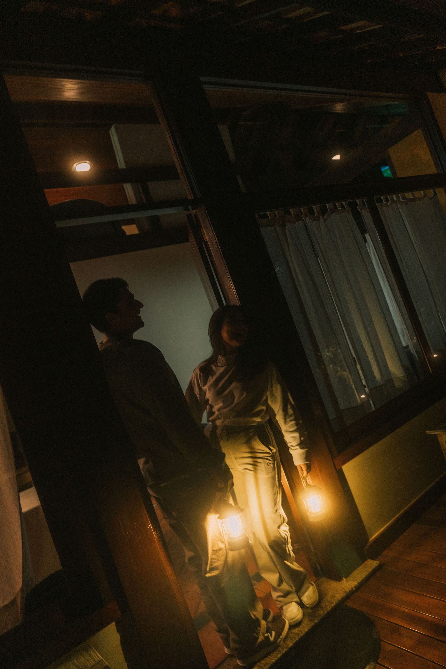 Dark and moody hallway scene lit by warm yellow lights creating dramatic shadows and silhouettes.