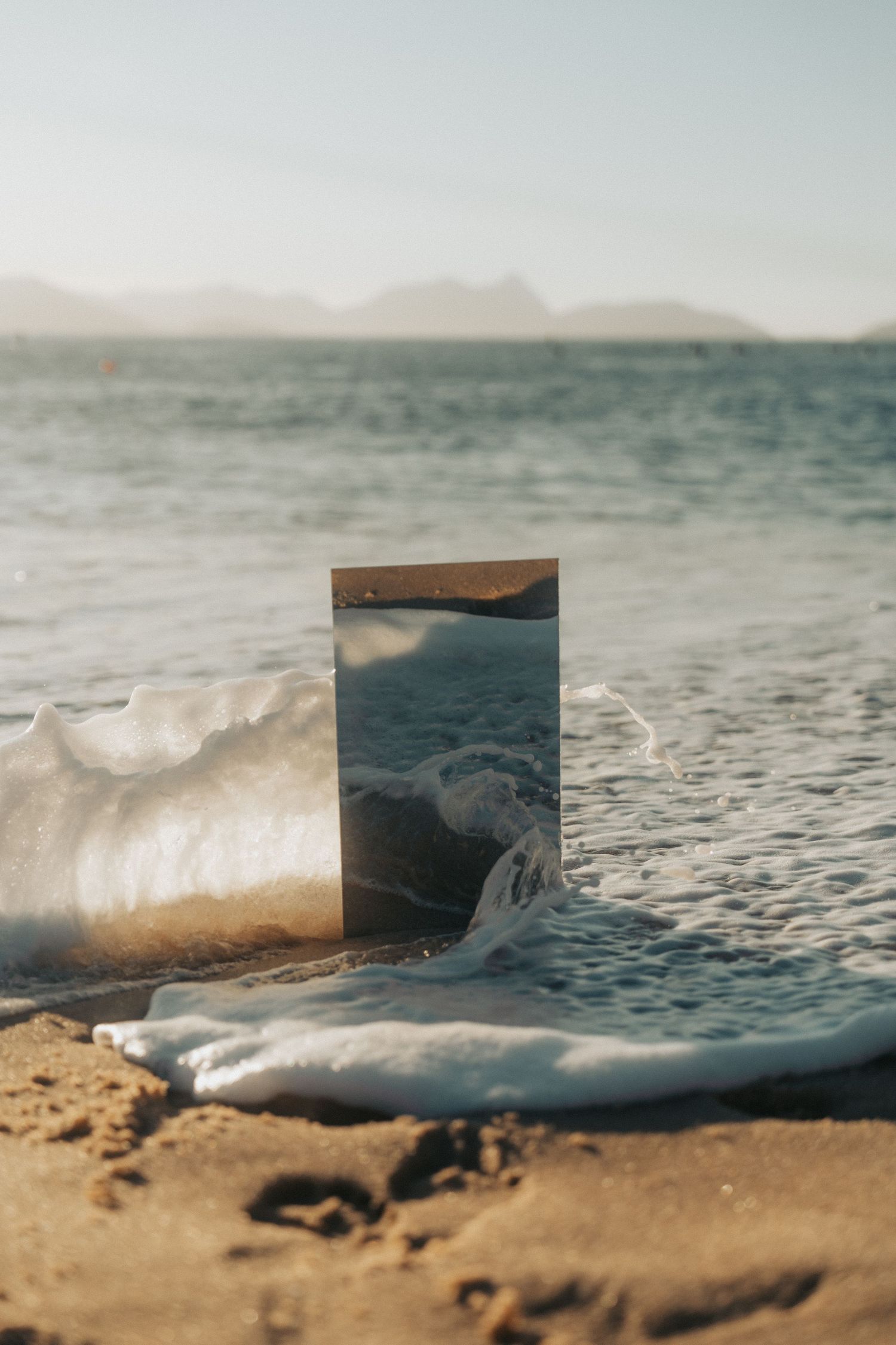 Close-up photos of melting ice chunks on sandy beach shore with soft focus and blurred background sea and sky.