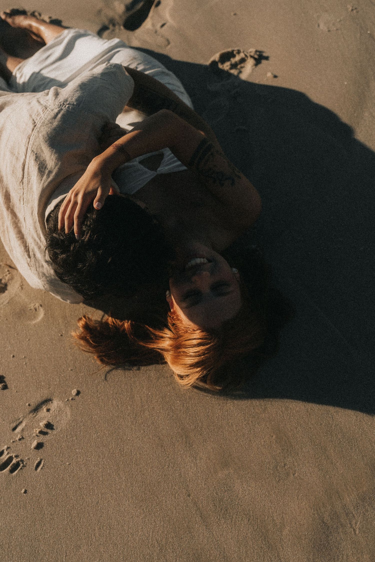 Artistic moody photo showing shadows and silhouettes of individuals lying on sandy beach texture.