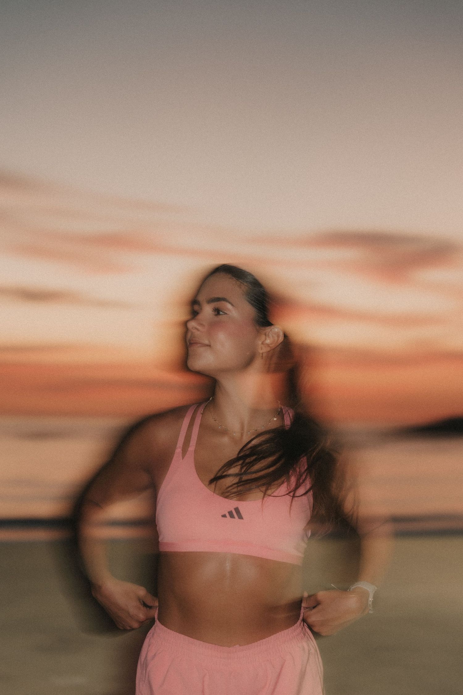 Person in pink sports bra dances against blurred sunset sky with dynamic motion effect creating dreamlike aesthetic.