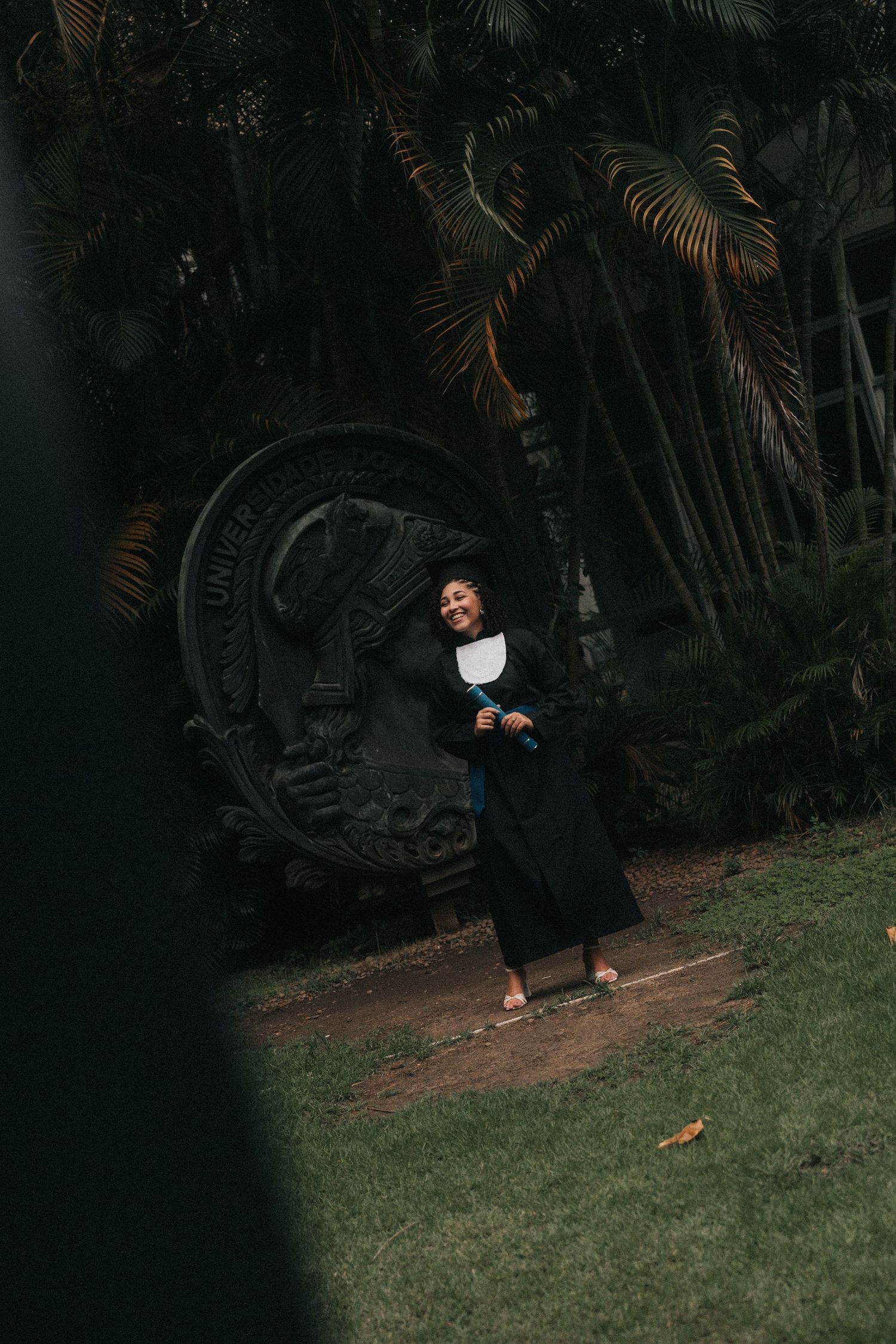 Person in dark clothing walks along a garden path with palm trees and ferns creating a tropical atmosphere.